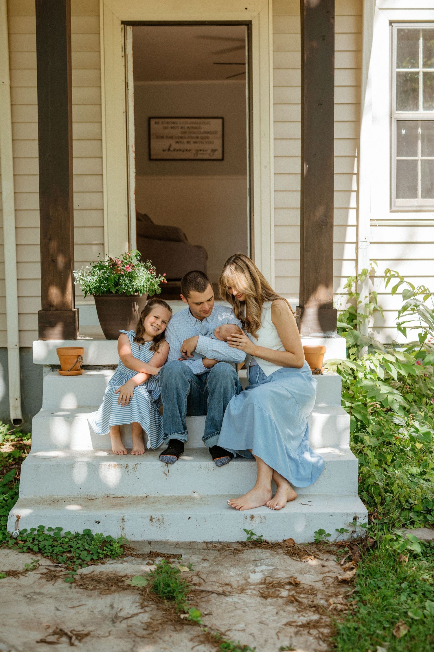 Family in coordinating blue outfits cuddles newborn on rustic white porch steps.