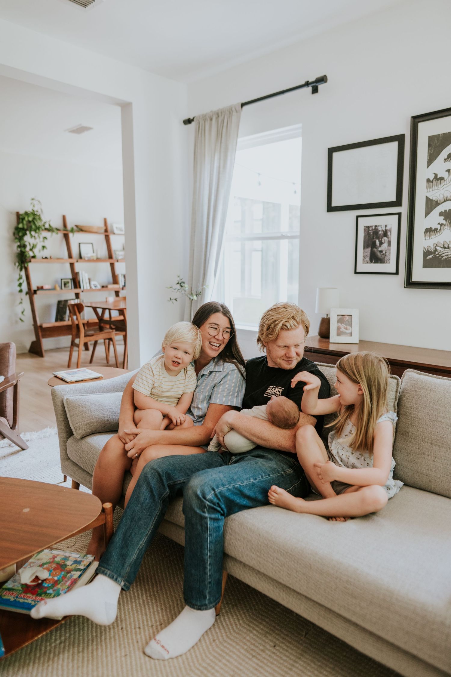 A loving family of five sits together on a couch, smiling and bonding with their newborn baby.