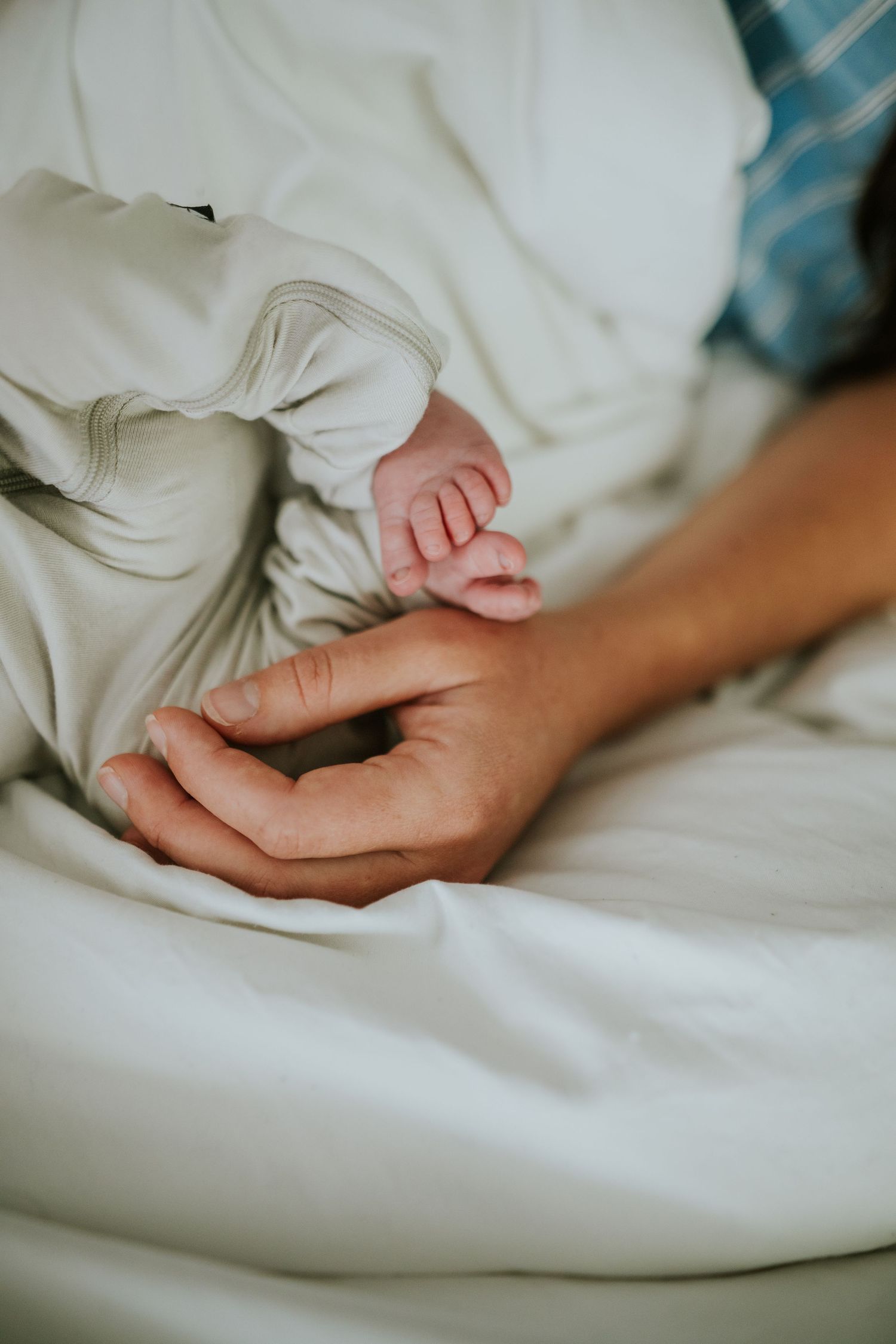 A parent's hand gently touches a newborn baby's tiny feet on a white bed.