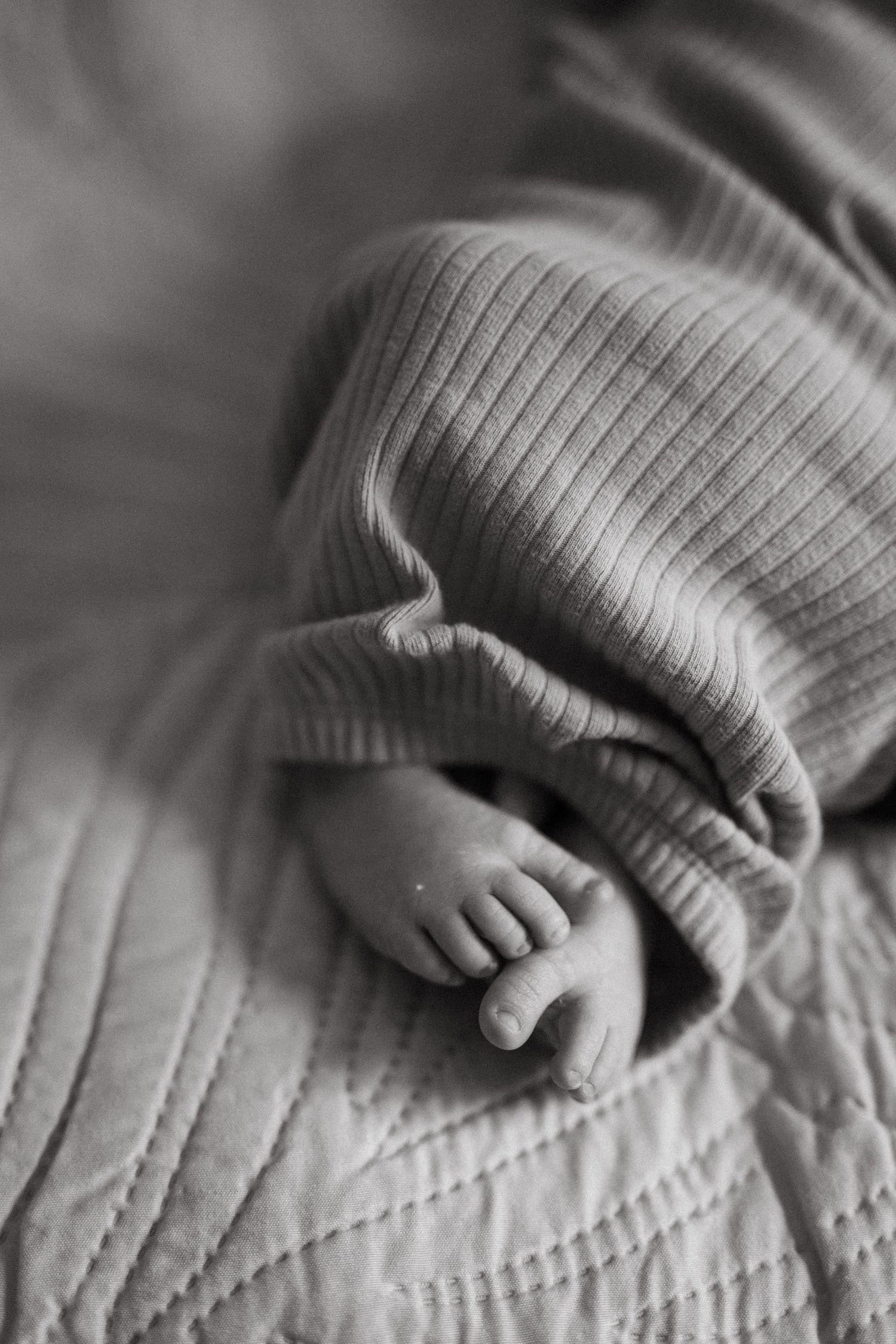 Black and white close-up of tiny newborn baby feet peeking out from ribbed blue outfit.