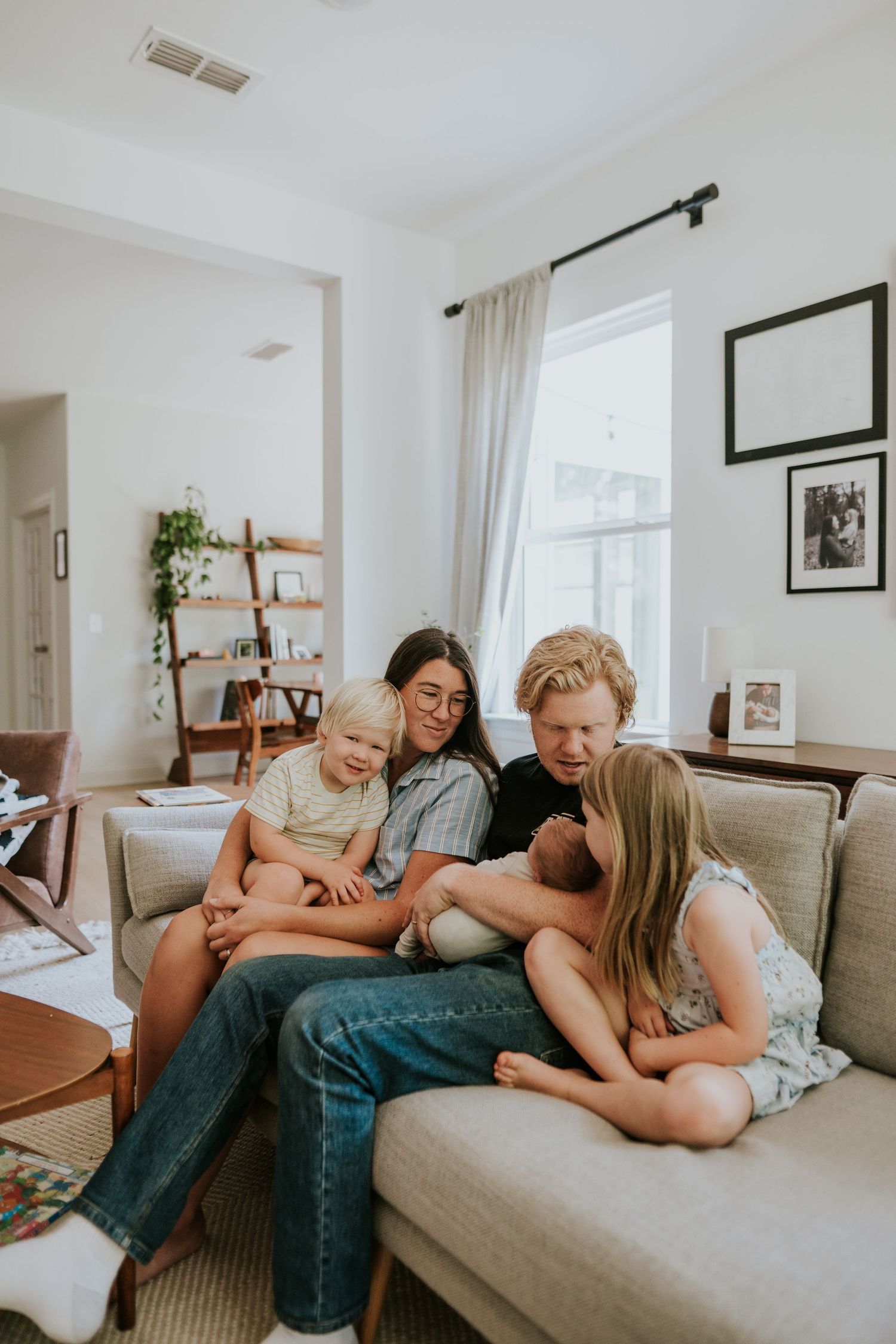A family of five gathers closely on a couch, looking down at their newborn baby together.