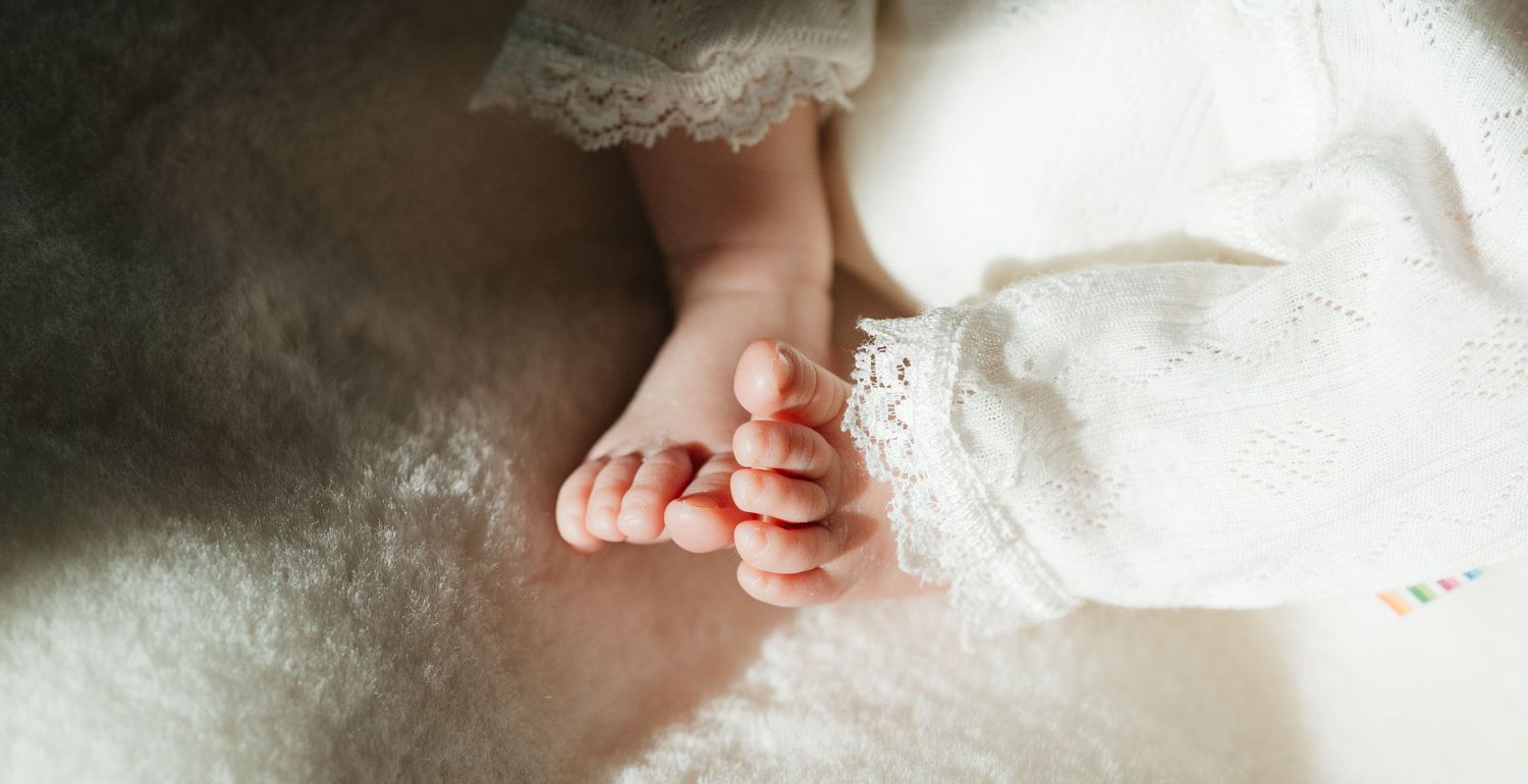 Close-up of a newborn baby's tiny feet and toes resting on a soft white blanket.