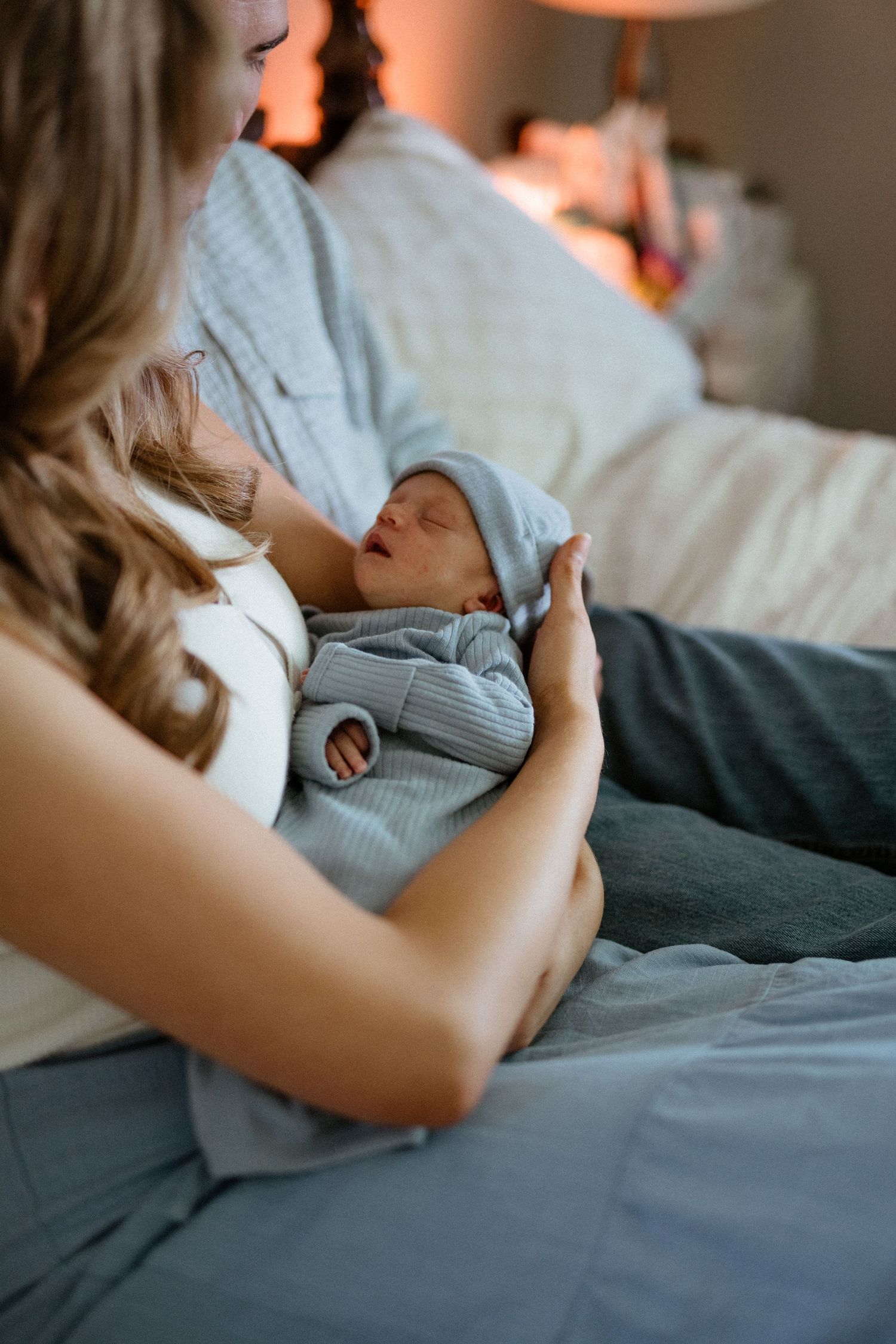Mother and father cradling sleeping newborn dressed in blue ribbed outfit on bed.