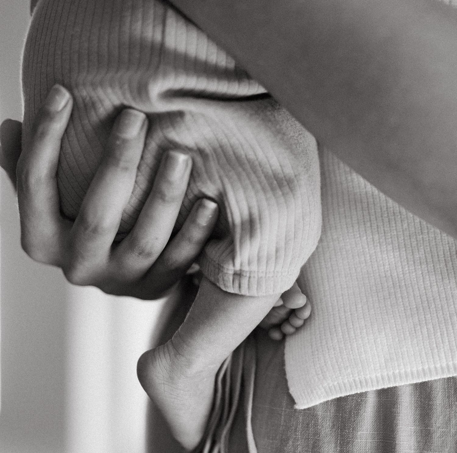 Black and white close-up of adult hand gently holding newborn baby feet.