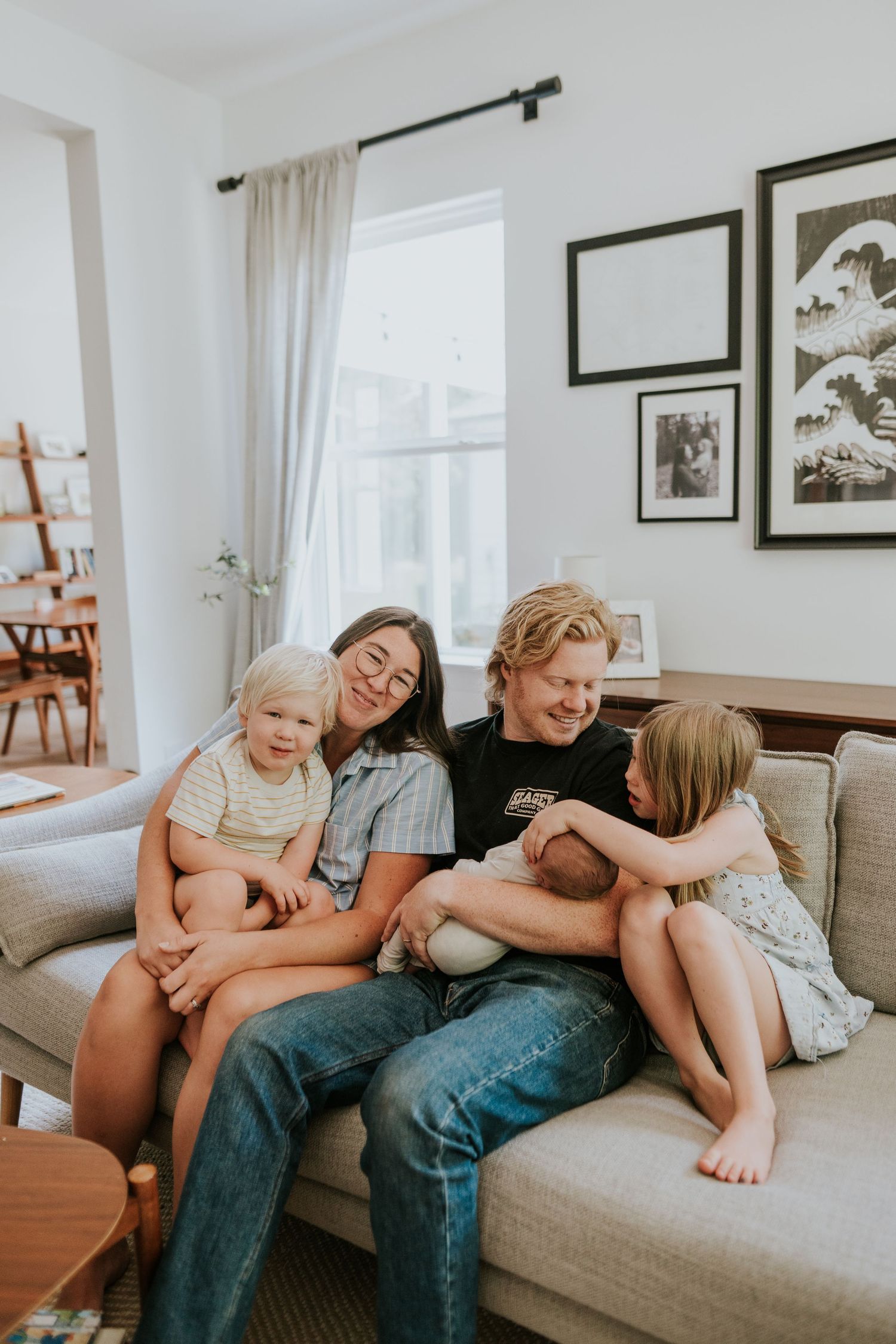 A happy family of four shares a joyful moment together on a gray couch in a bright living room.