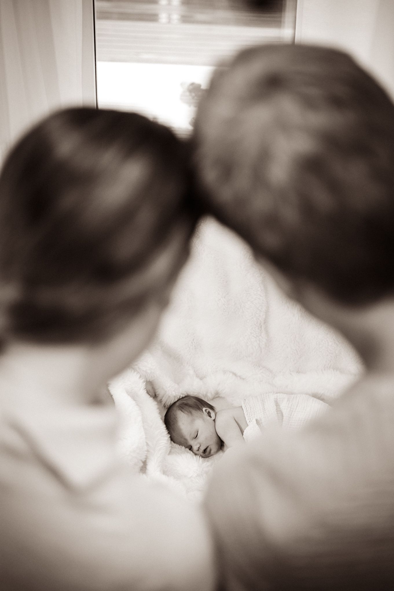 New born kuvaus. Lapsi makaa sohvalla ja hänestä on söpö kuva. Vanhemmat katselevat lasta rakastavasti.