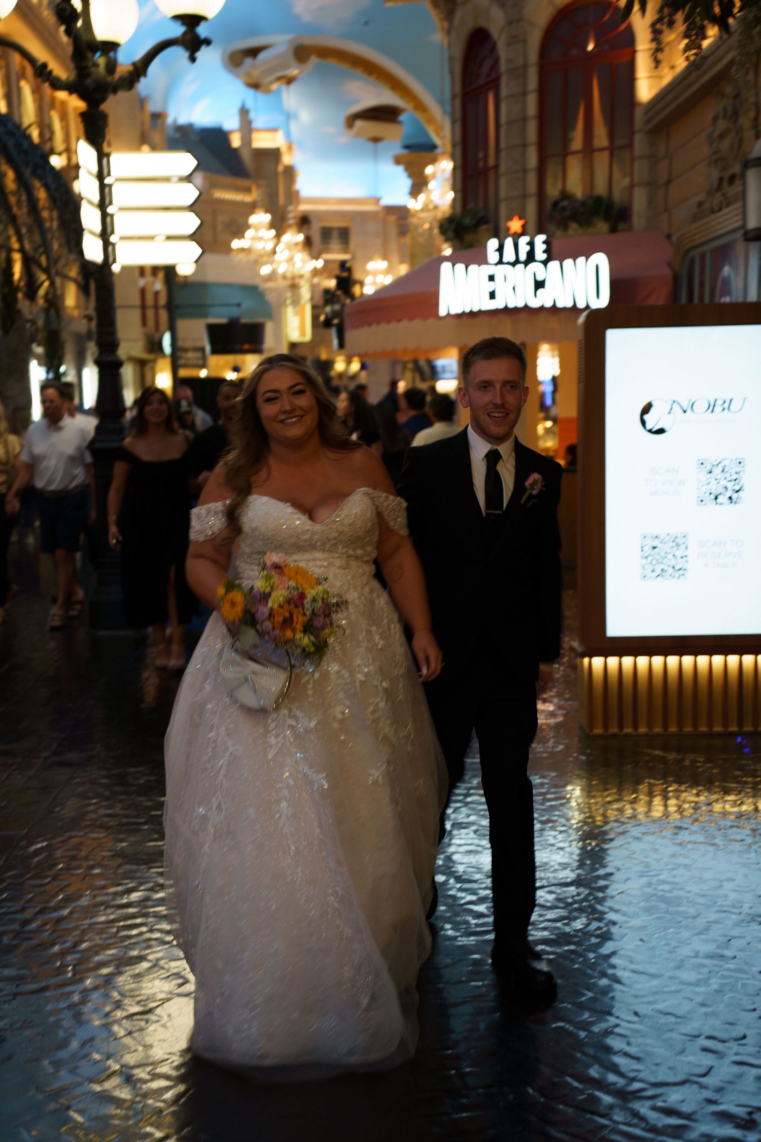 Newlyweds walk together near Cafe Americano in Las Vegas, bride holding yellow floral bouquet.