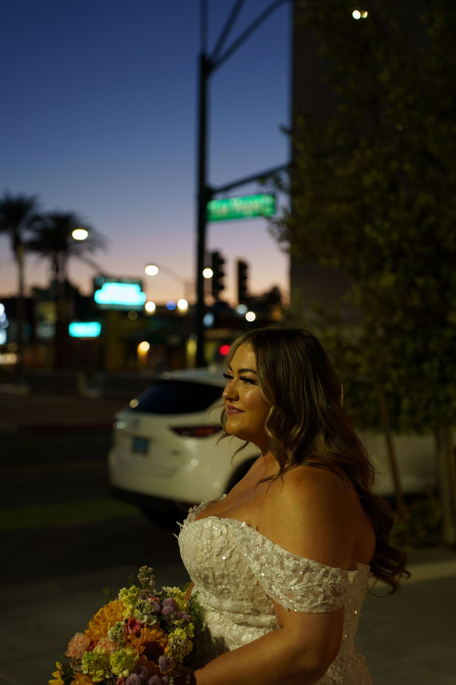 Bride in off-shoulder lace gown holds colorful bouquet at night on a Las Vegas street.