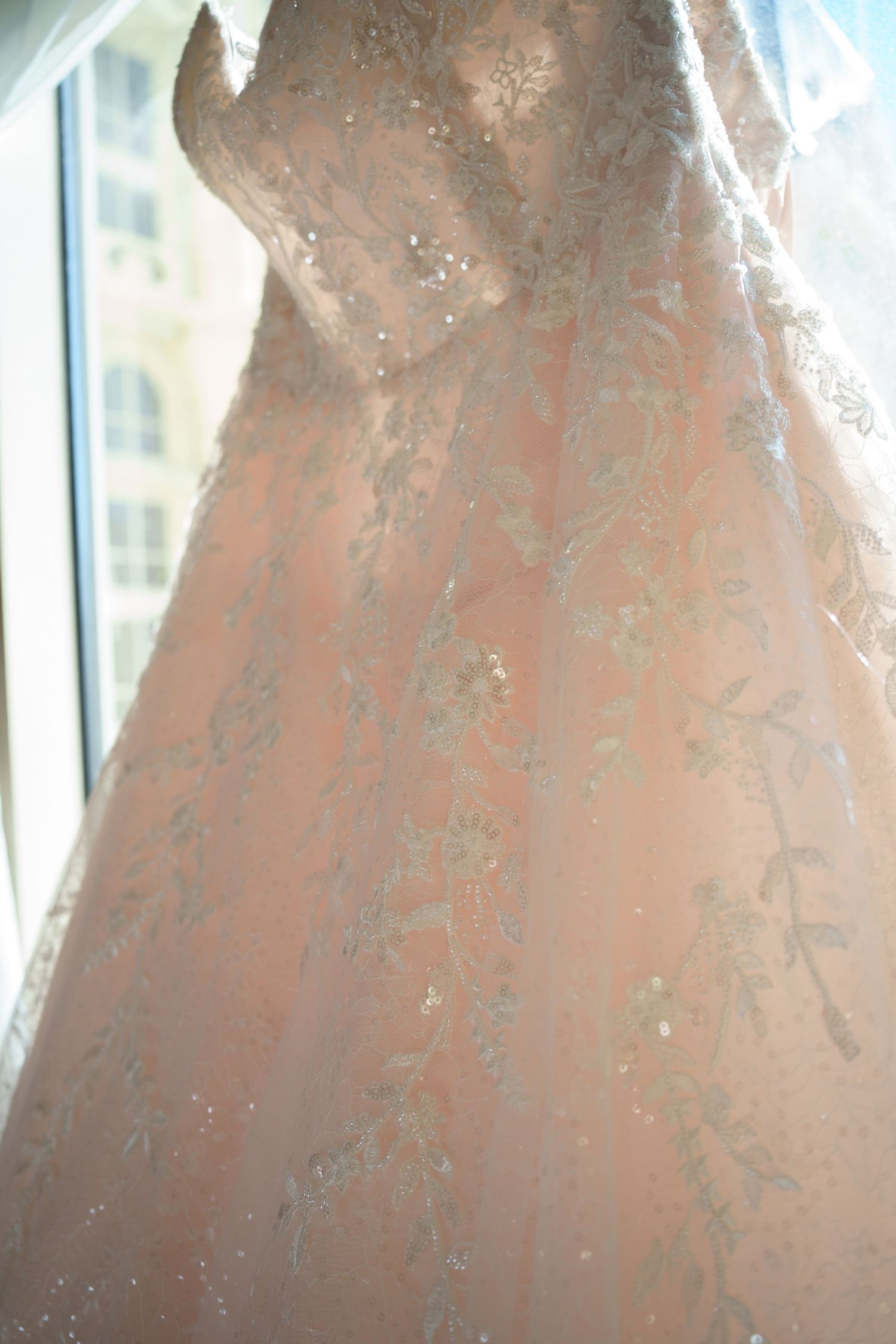 Close-up of a blush pink lace wedding gown with silver floral embroidery and sequin details.