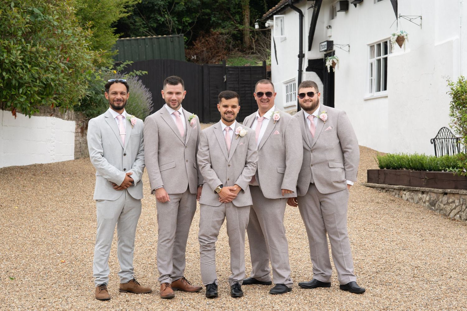 Groom and groomsmen posing in matching grey suits with pink ties outdoors.