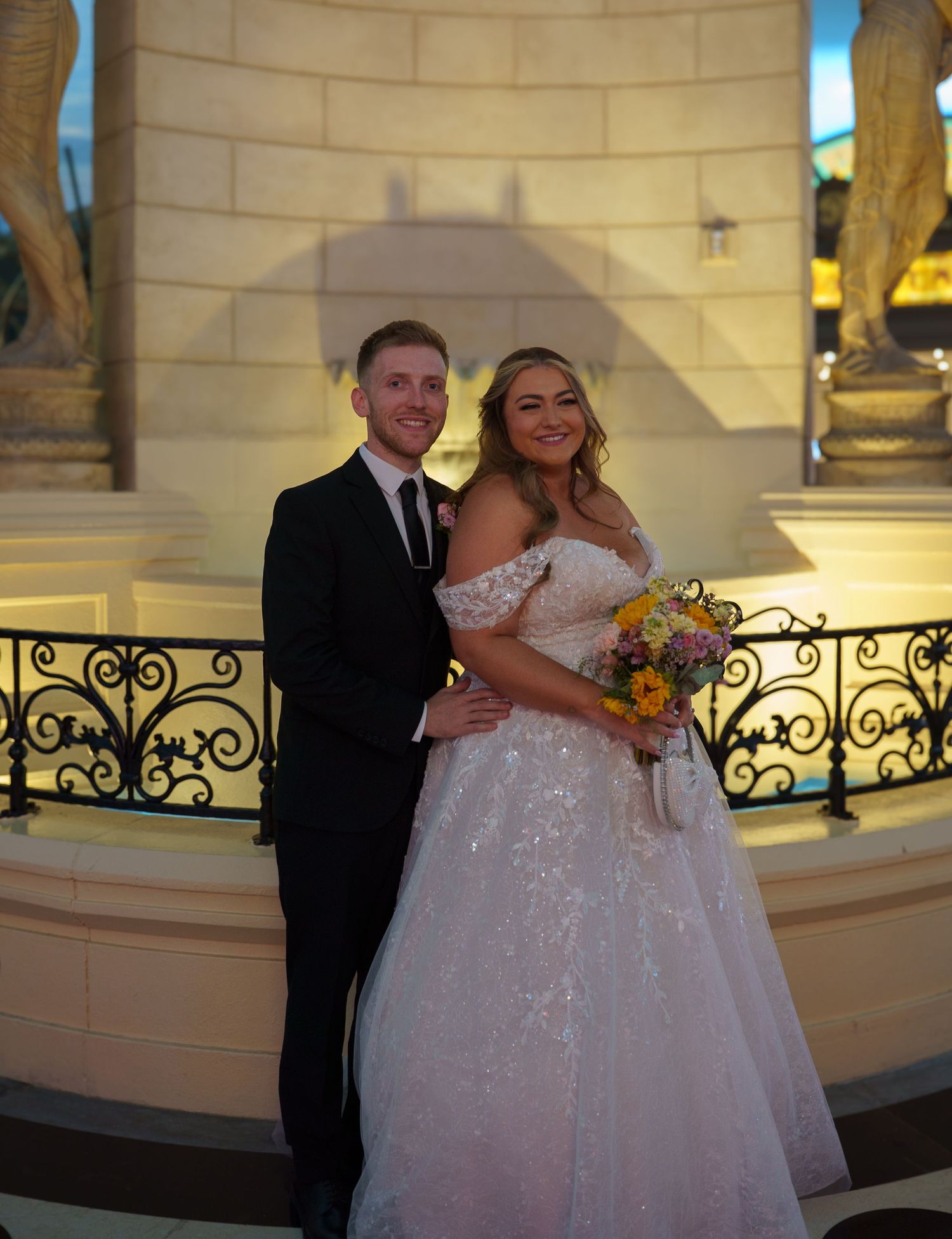Bride and groom posing together in front of ornate fountain at Las Vegas wedding venue.