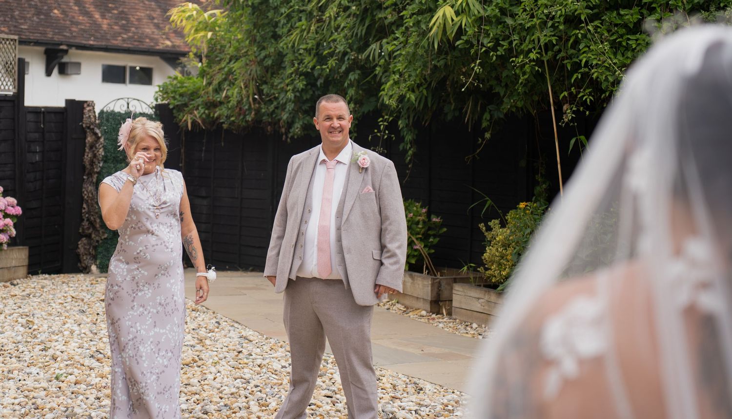 Parents of bride smiling as they see bride in wedding dress outdoors.