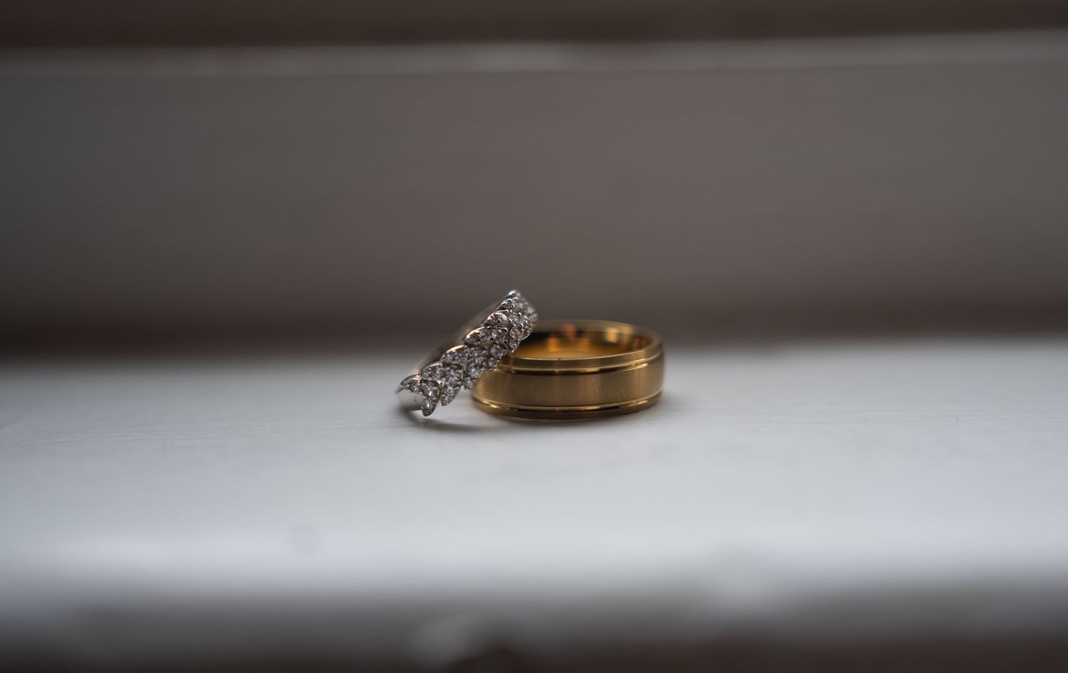Gold and silver diamond wedding bands resting on a white windowsill.