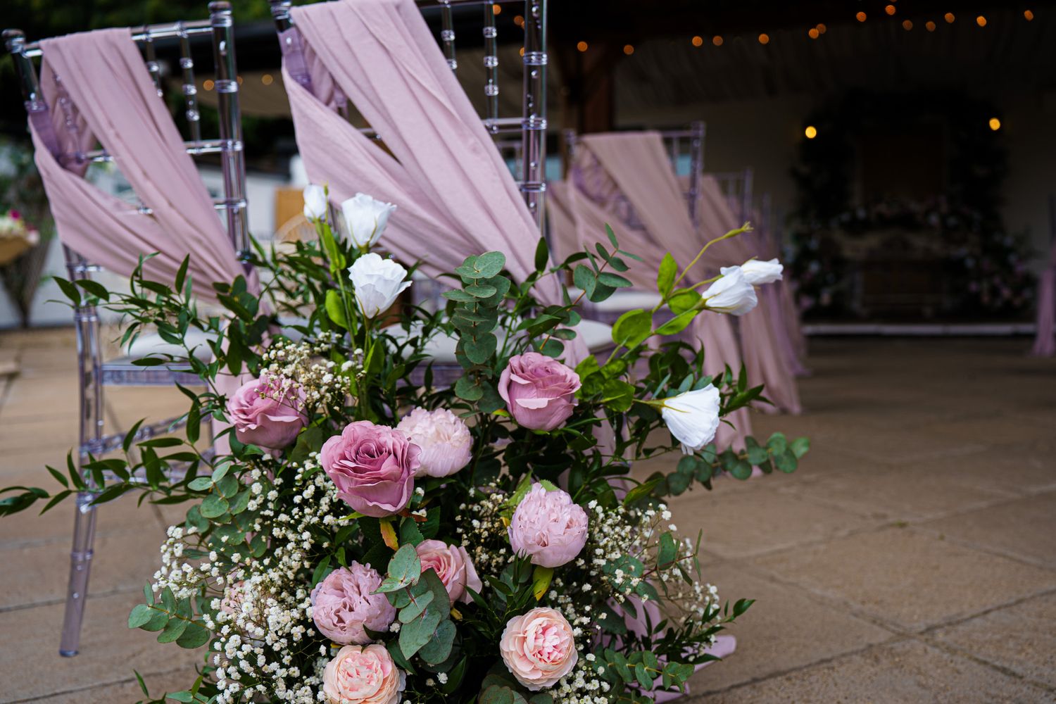 Pink roses and white flowers wedding ceremony aisle arrangement with draped blush fabric chairs.