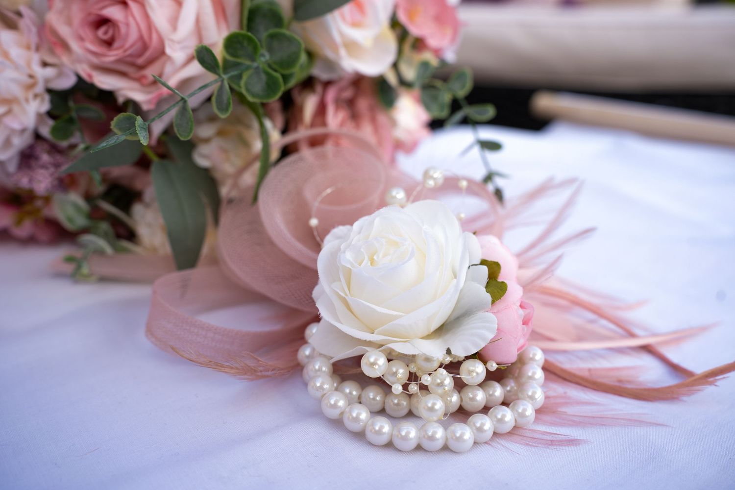 Elegant pearl bracelet wrist corsage with white rose and pink ribbon for a wedding.