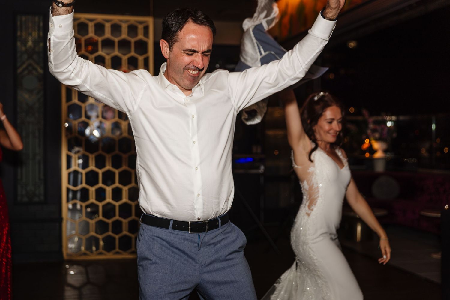 Wedding guests dancing energetically with arms raised at the reception party.