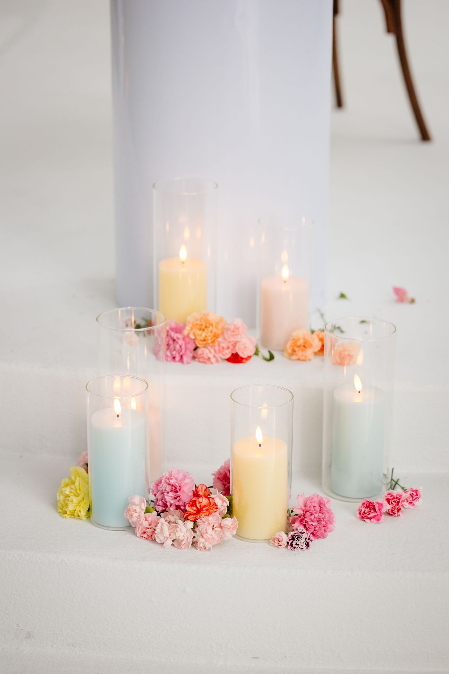 Elegant candle centerpiece with pastel flowers and glass hurricane vases on white surface.