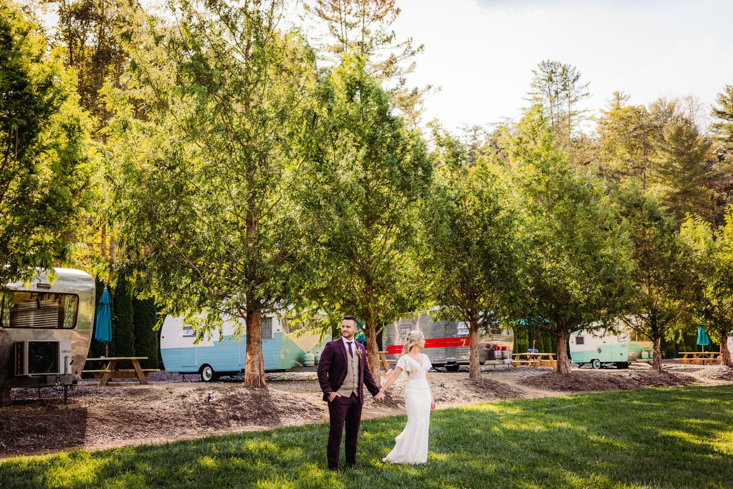 A couple stands together in a scenic campground surrounded by tall green trees.