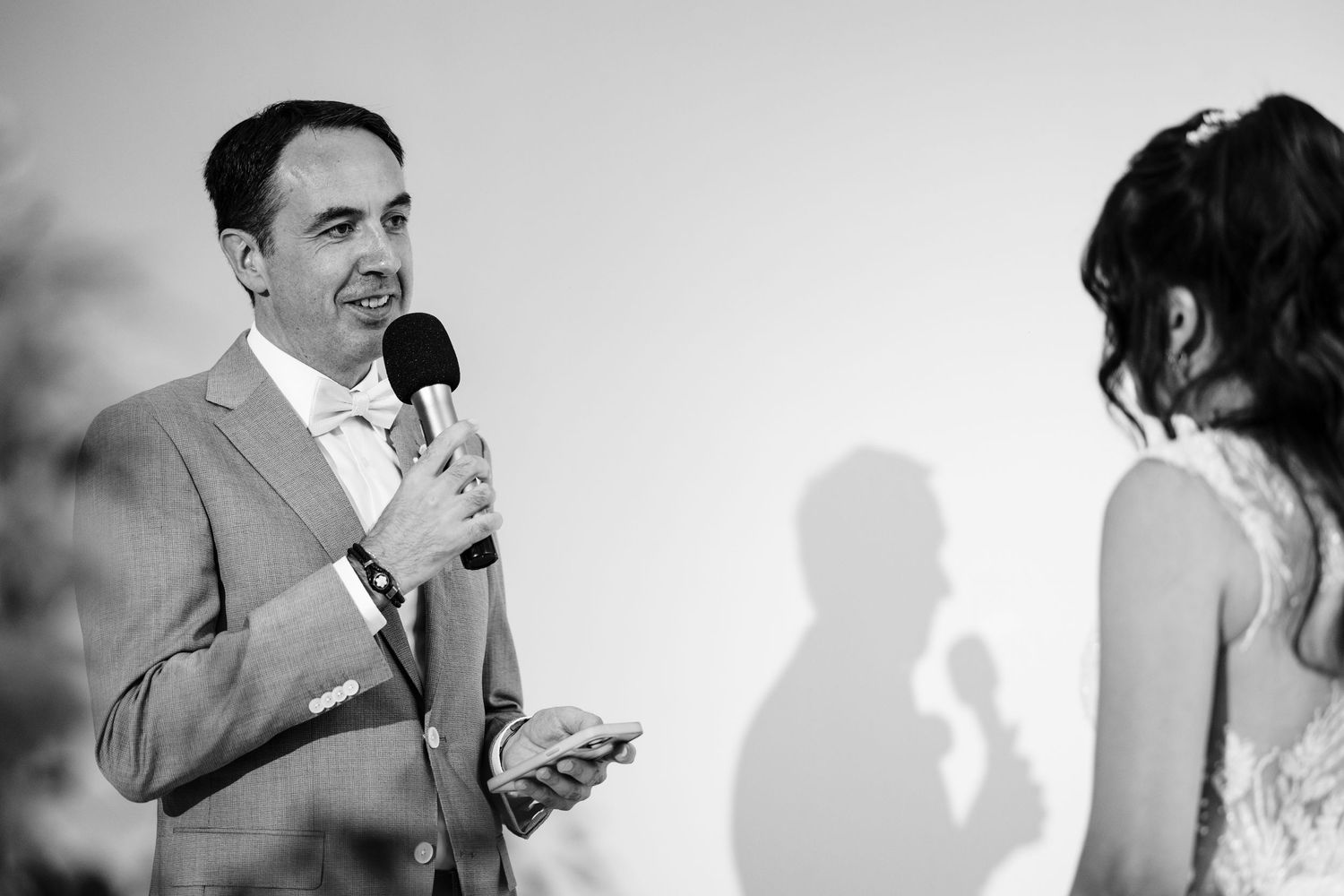 A person in a gray suit speaks into a microphone during a wedding ceremony.
