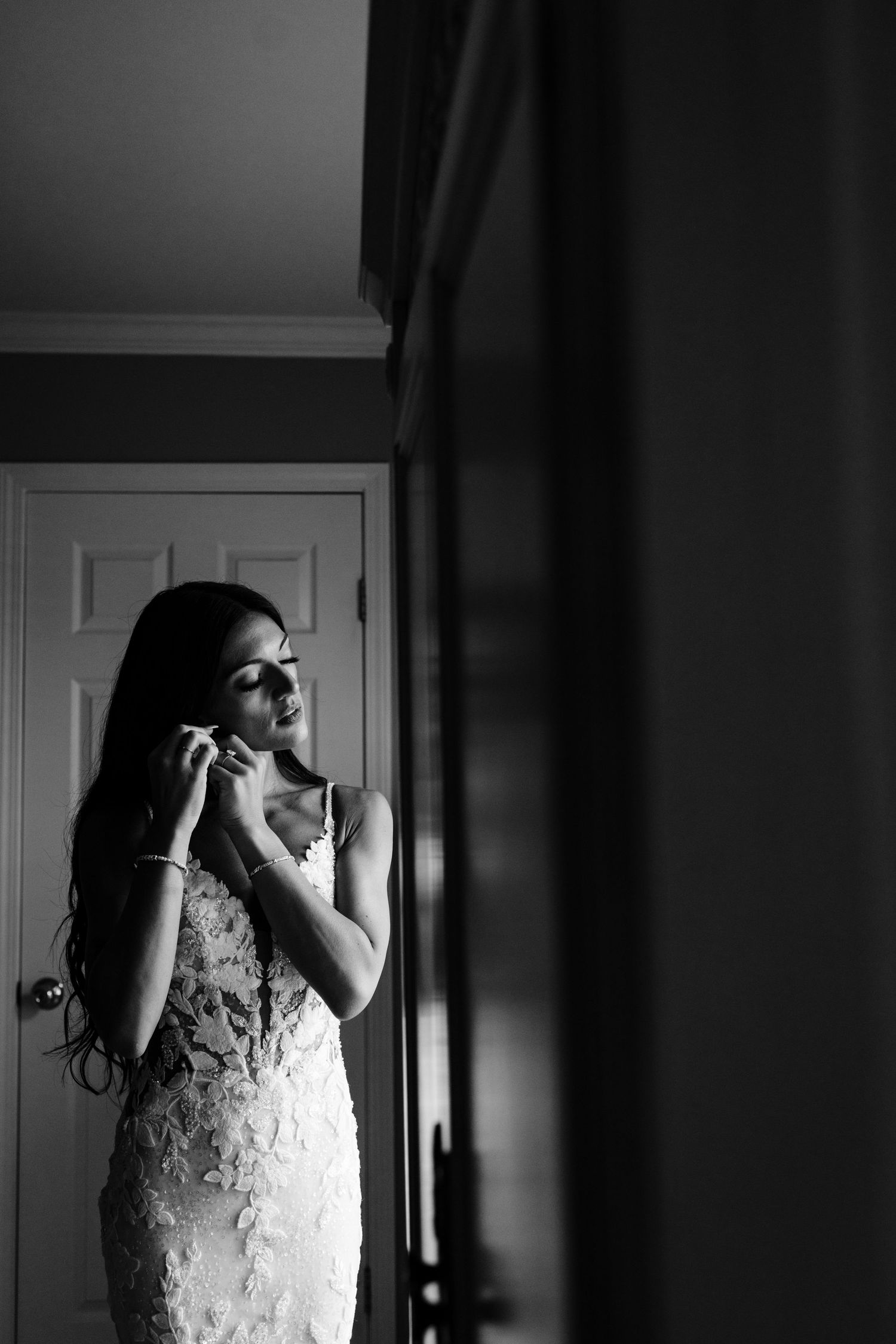 Dramatic black and white photos show a bride getting ready in low-lit room with flowing dress.