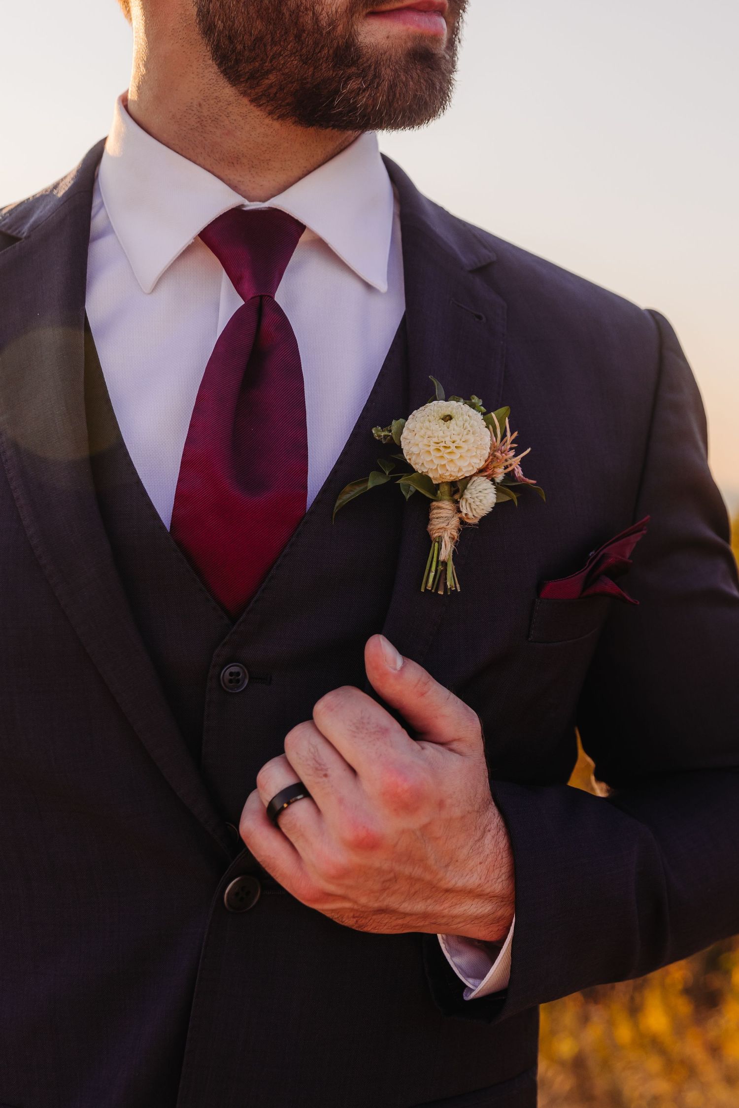 Close-up of groom's burgundy tie and boutonniere against dark suit jacket.