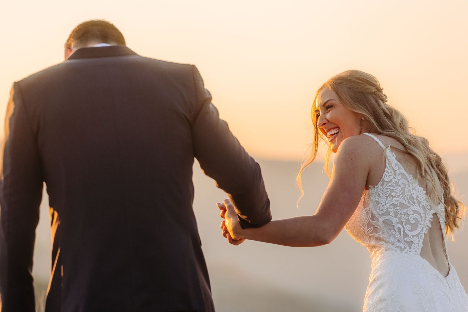 Wedding couple silhouetted against warm sunset light on a mountaintop with glowing skies.