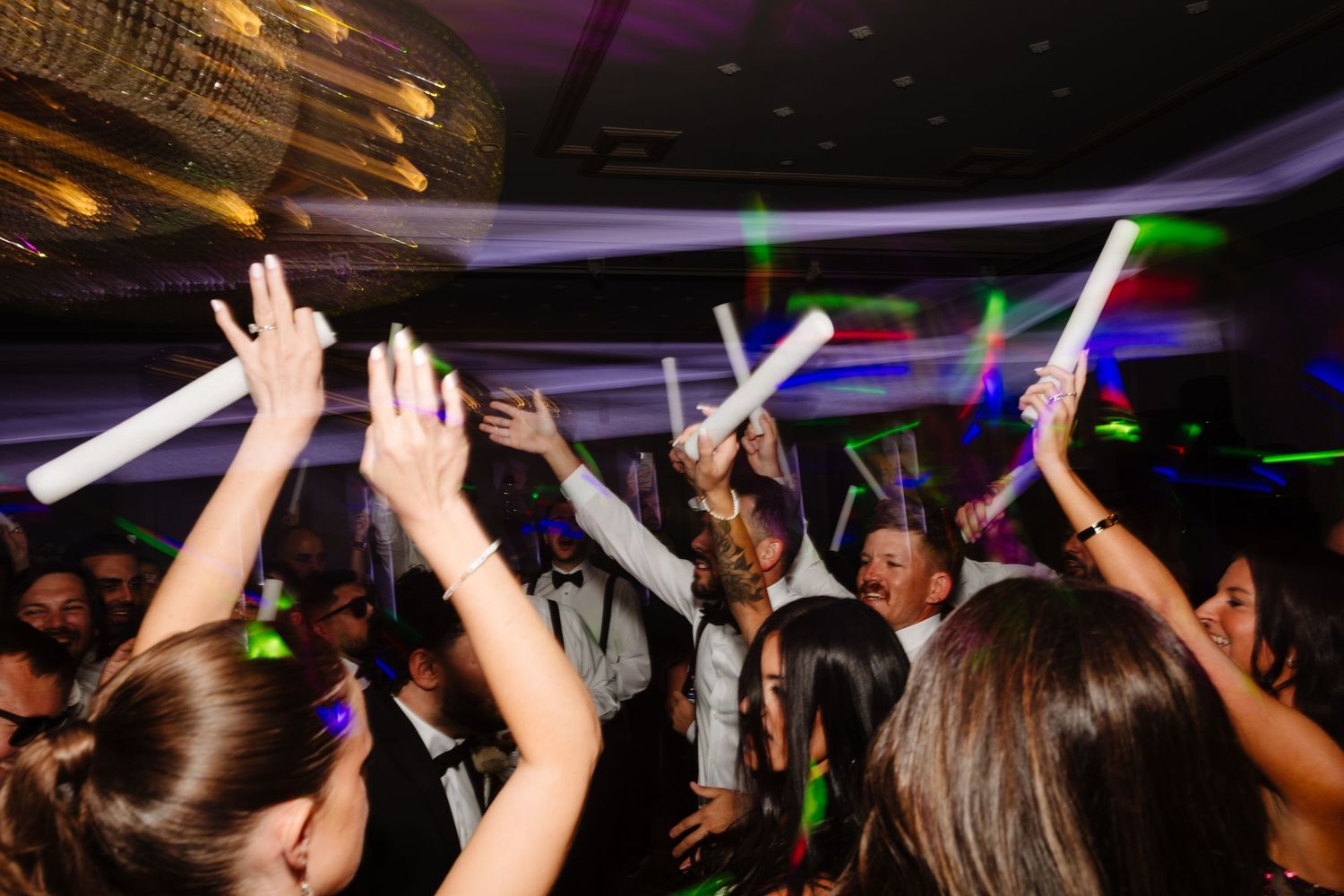Lively dance floor filled with celebration and raised hands under purple ambient lighting.