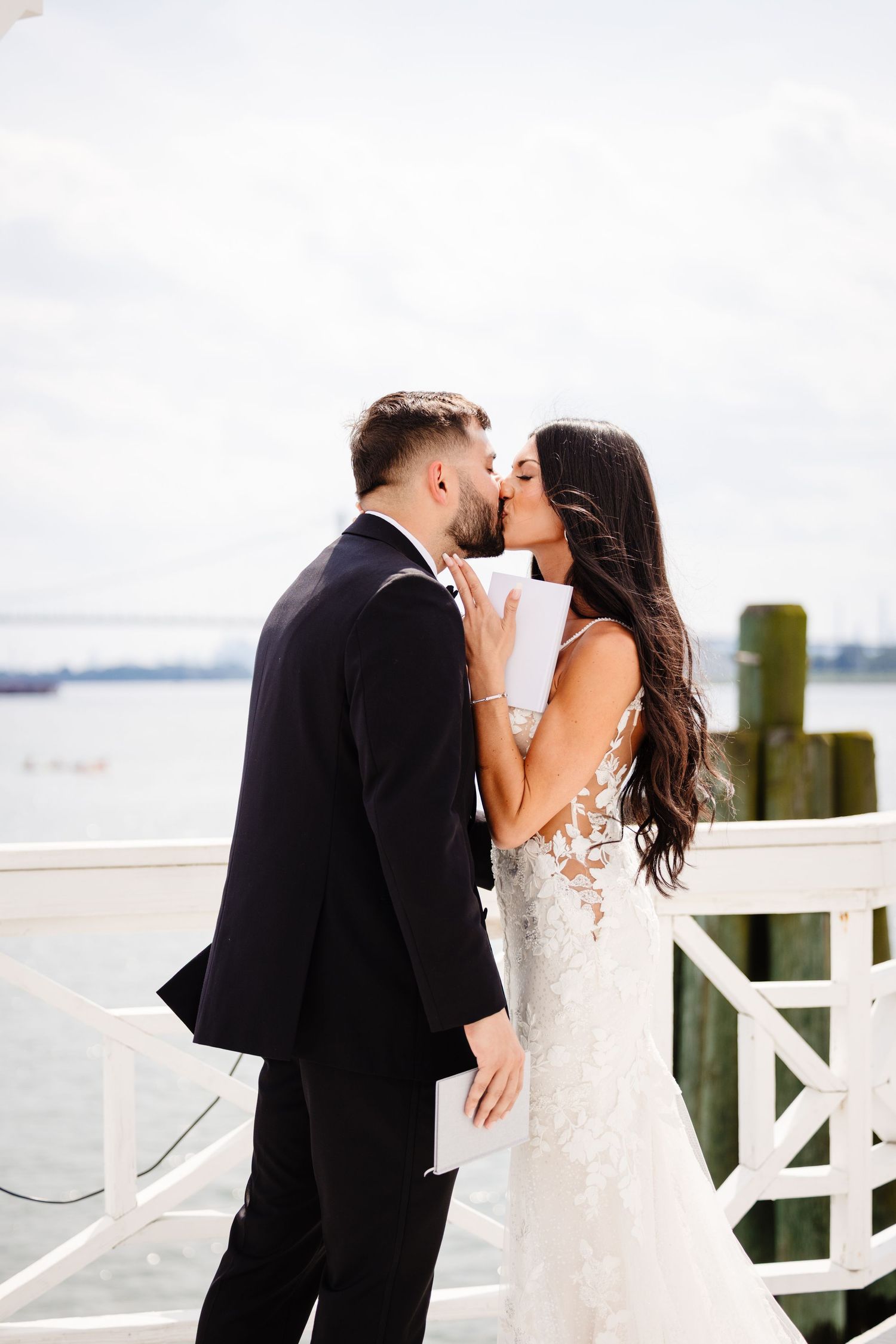 Newlyweds share their first kiss as husband and wife on a waterfront deck.