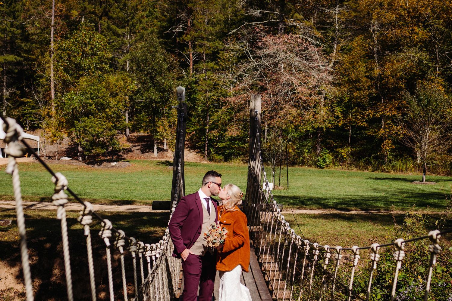 A couple stands on a suspended rope bridge during an autumn outdoor photo session.