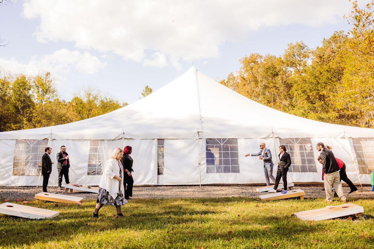 A white wedding tent set up outdoors with guests mingling on a sunny autumn day.