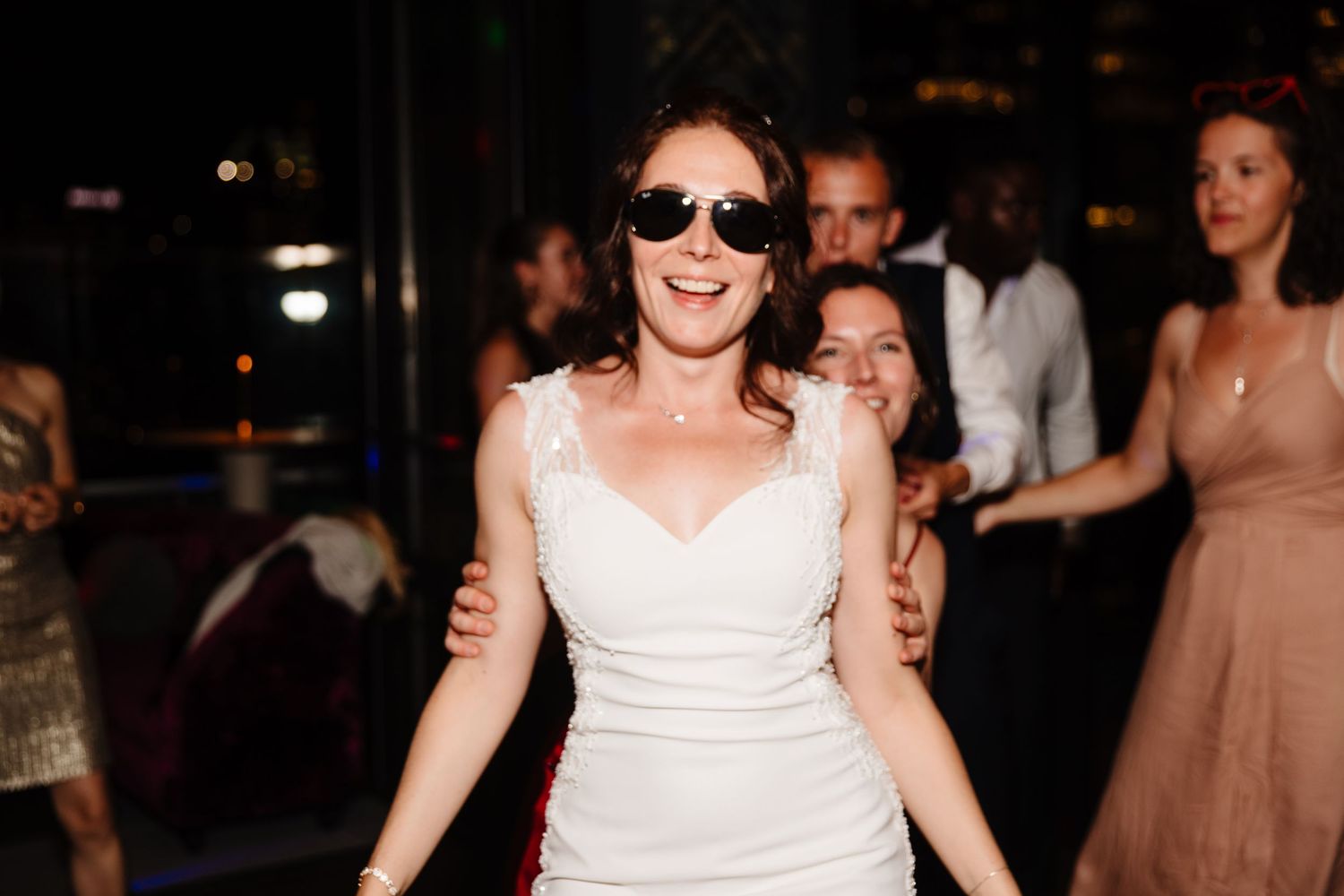 Joyful bride wearing sunglasses dances and celebrates during her wedding reception.