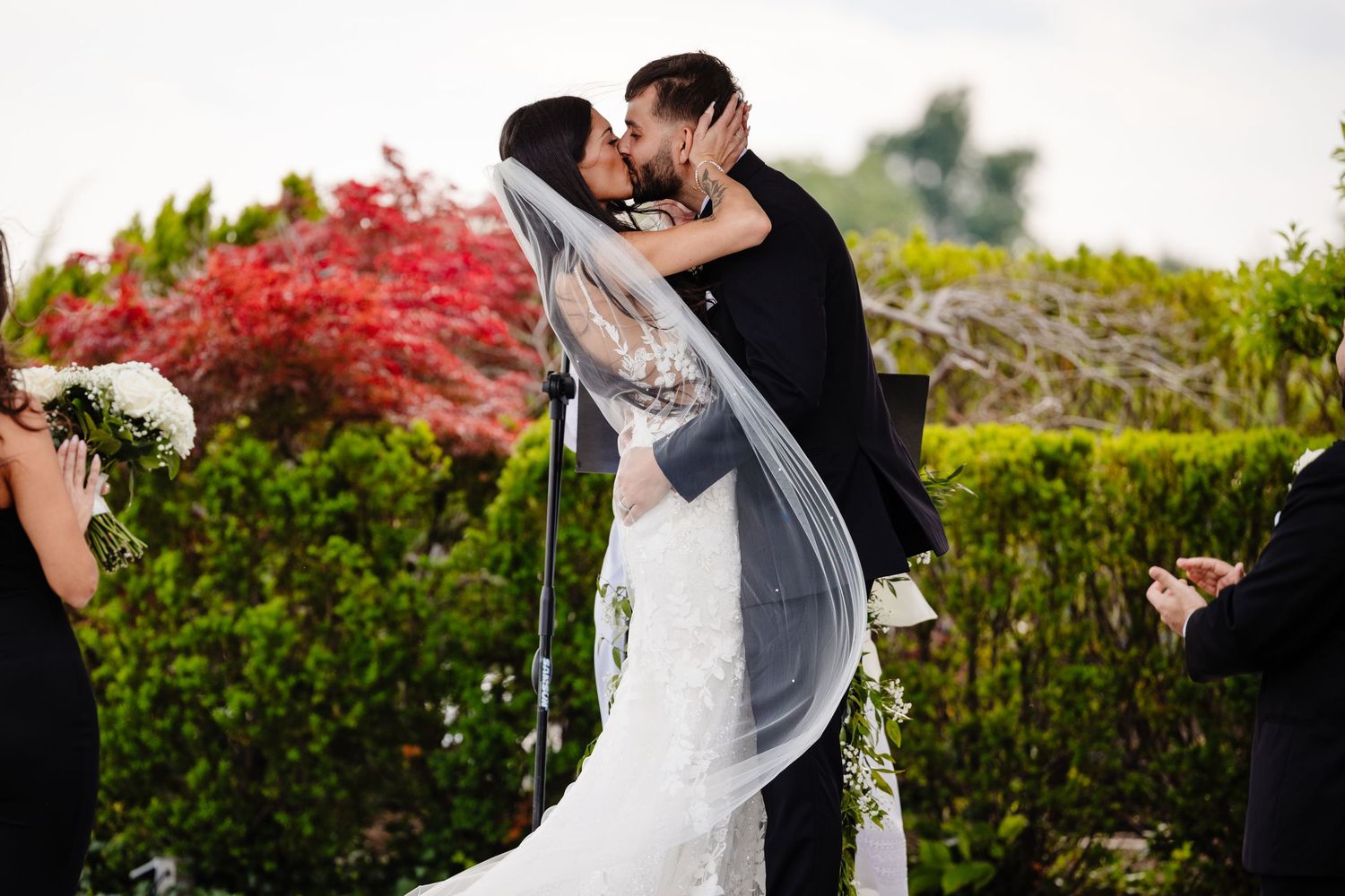Wedding couple embracing under blooming red foliage on a scenic garden path.