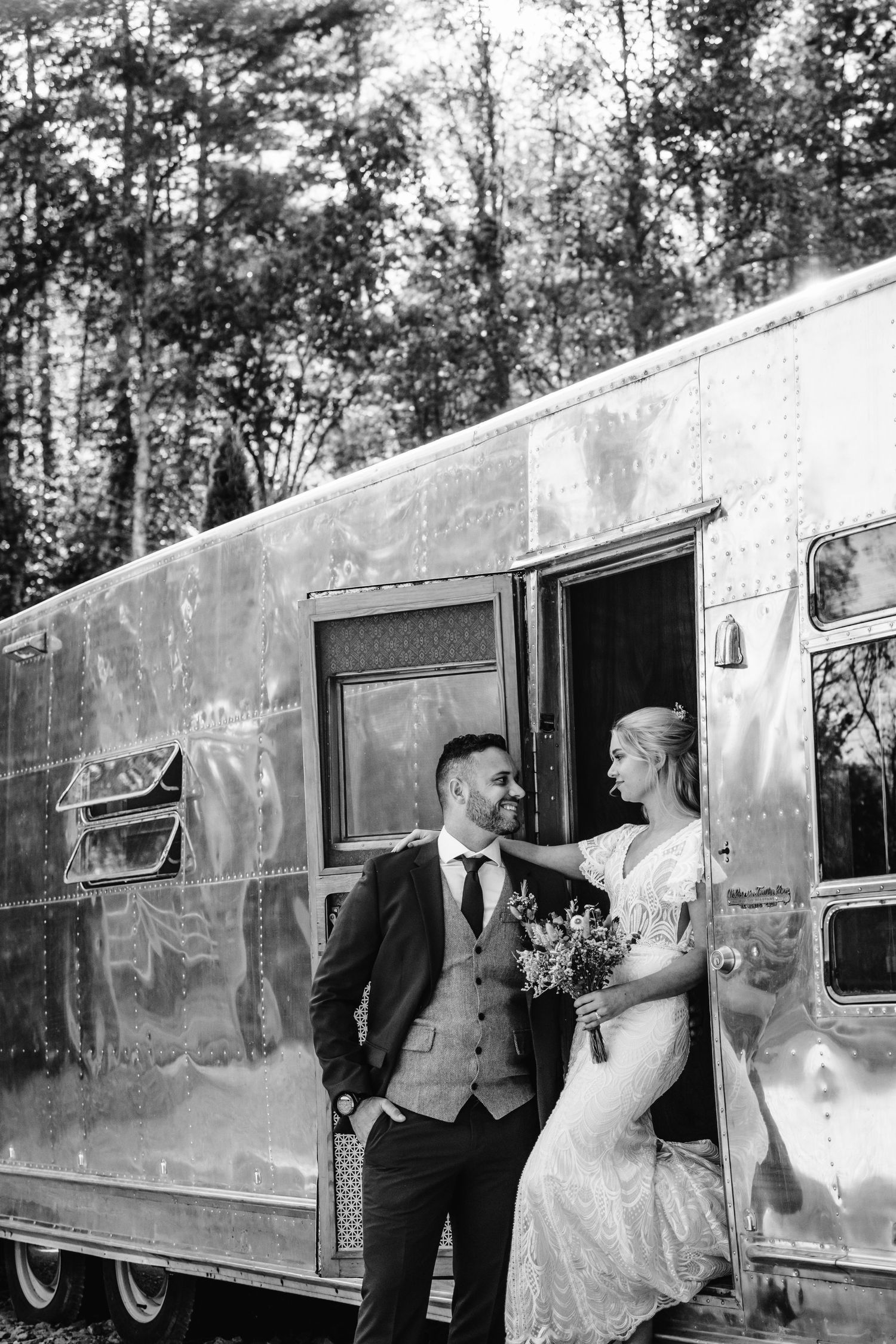 A classic black and white portrait of a couple posing beside their vintage Airstream trailer.