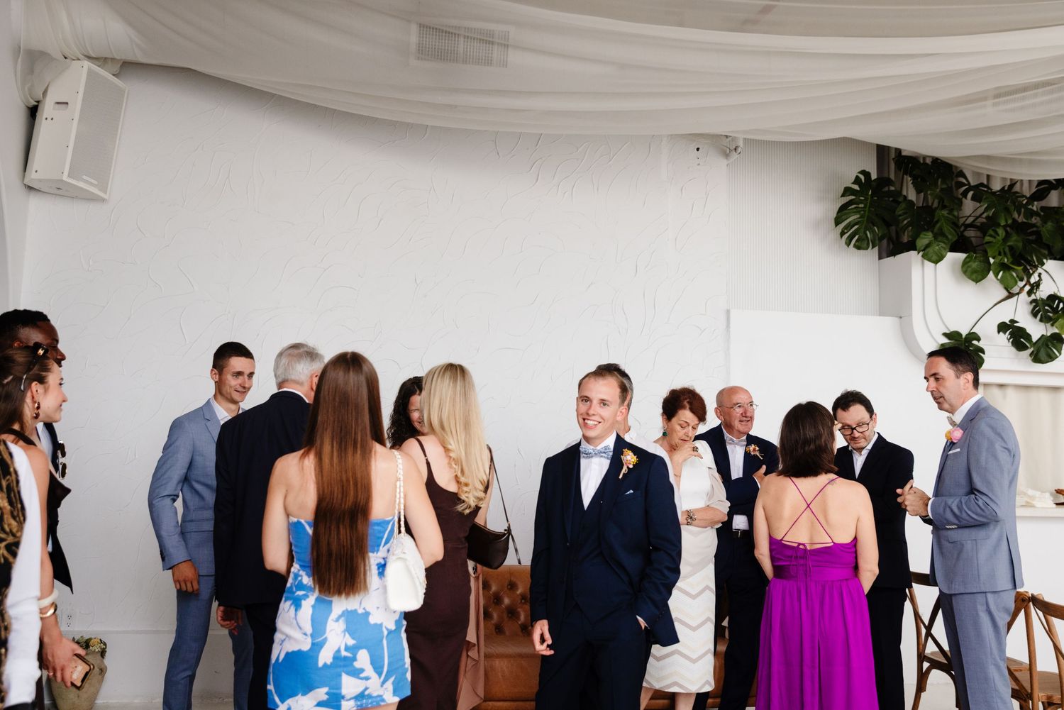 Wedding guests socializing in a white-draped venue space.