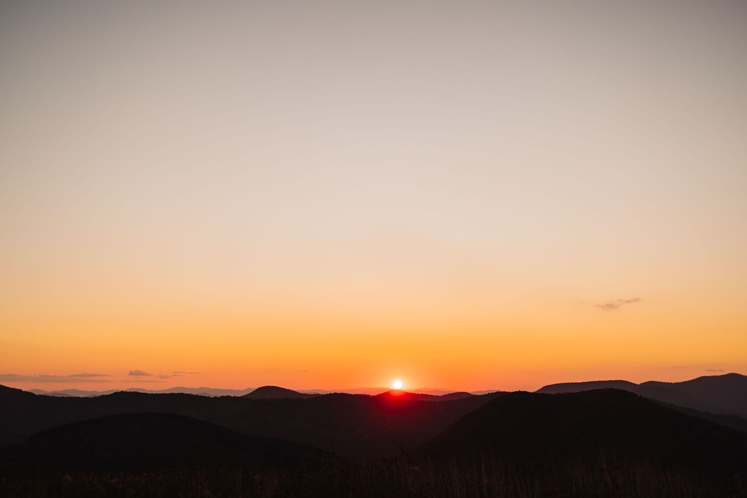 Dramatic mountain sunset with silhouetted peaks against an orange sky.