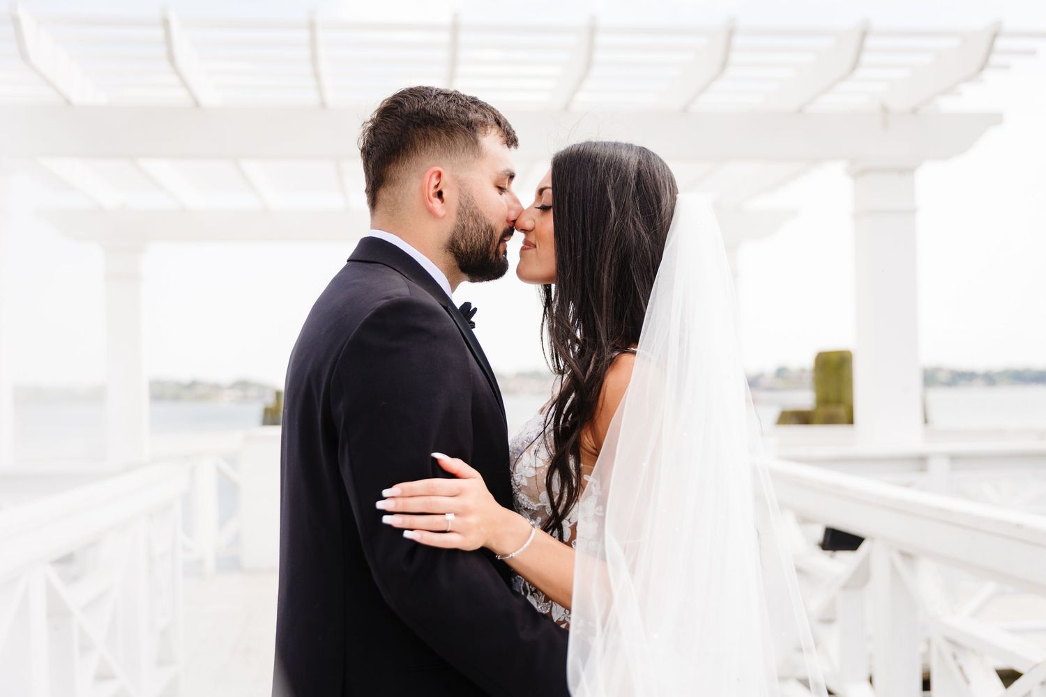 Newlyweds embrace intimately under a white pergola during their wedding day photoshoot.