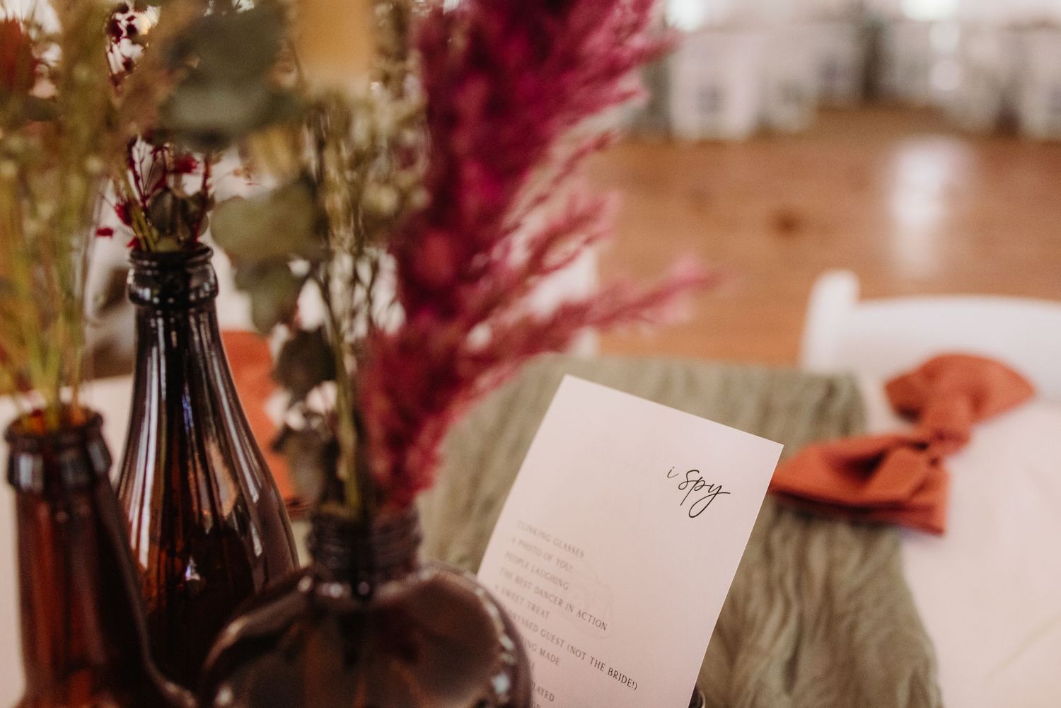 Wedding reception detail with dark bottles, dried flowers and paper menu on decorated table.