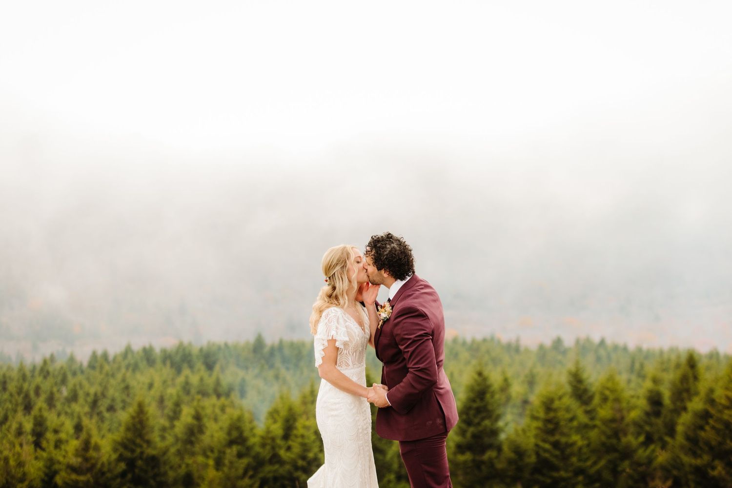 A romantic wedding ceremony moment captured against misty mountain peaks and evergreen forests.