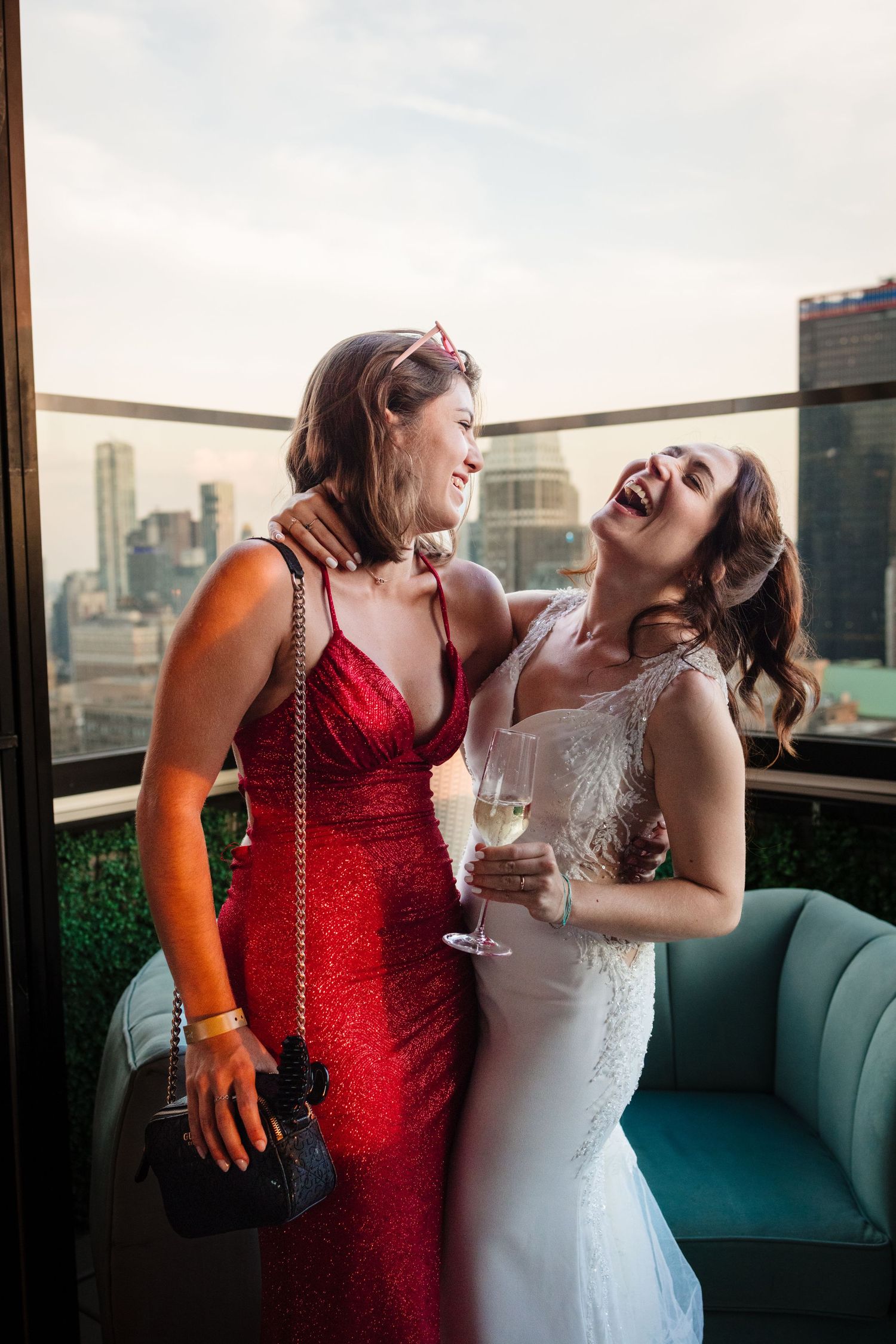 Two wedding guests sharing joyful moment on rooftop terrace with NYC skyline backdrop.