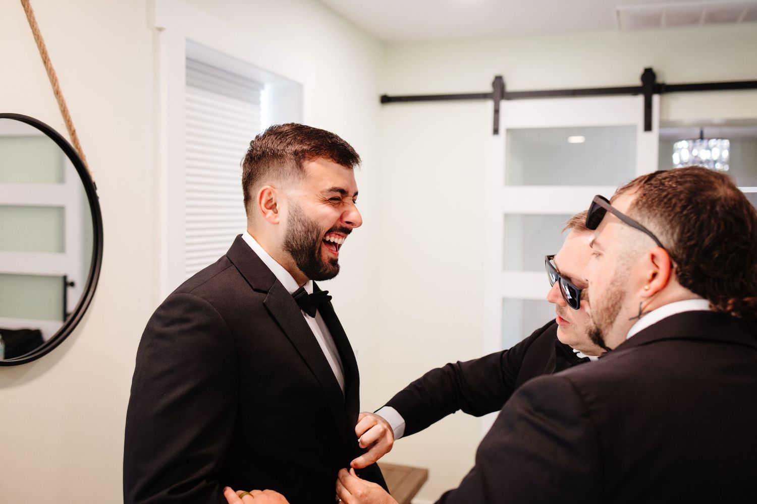Groomsmen help each other with bow ties and preparations in a bright room.