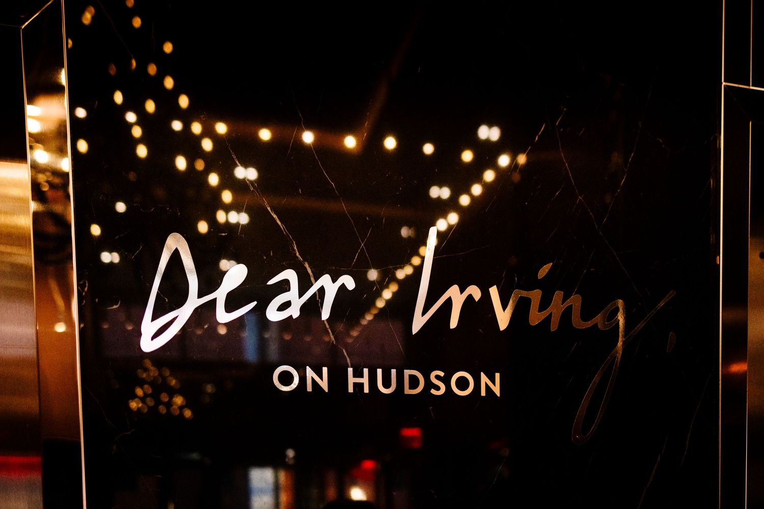 Illuminated sign for Dear Irving on Hudson with string lights in background.
