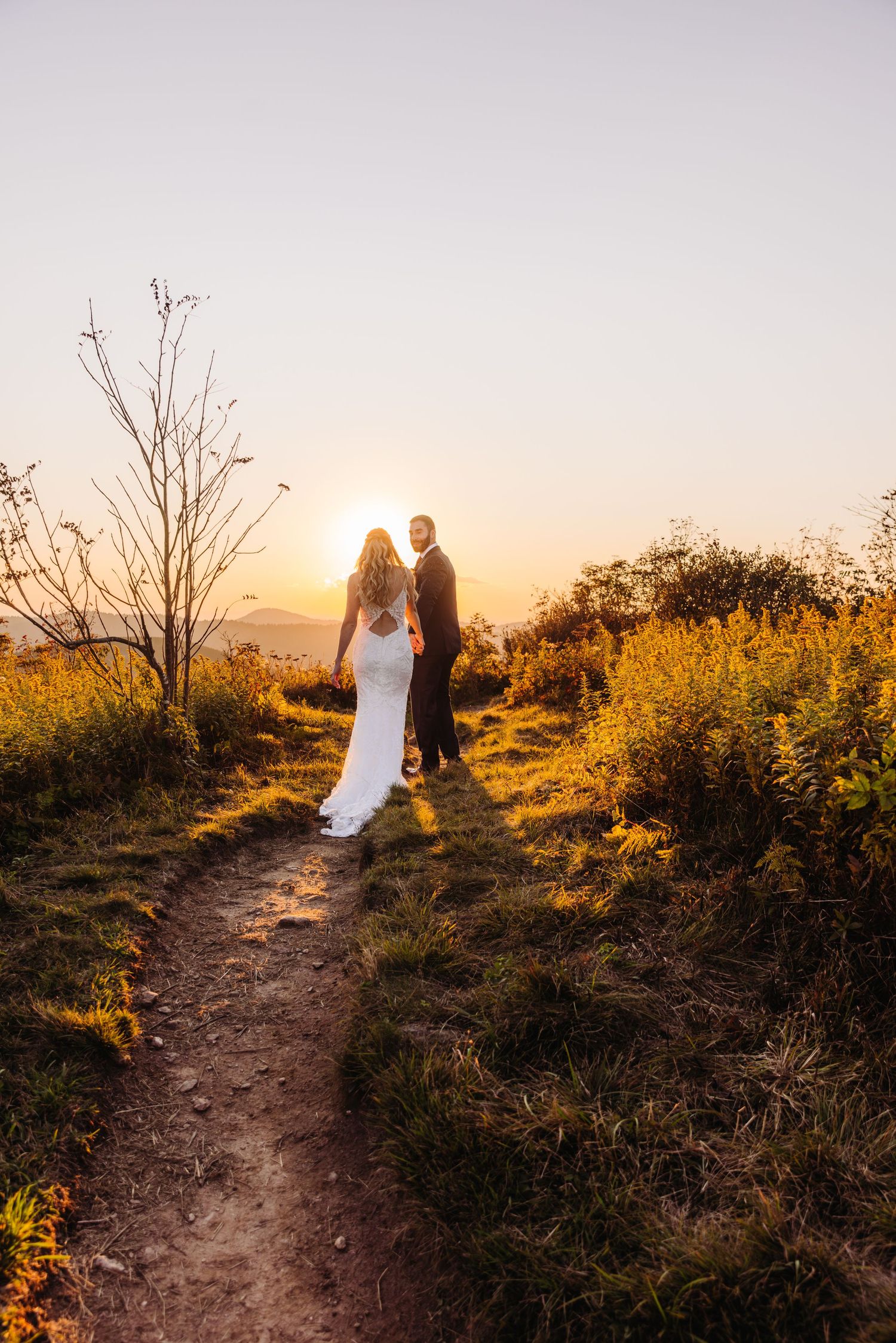 Romantic sunset wedding portrait on a scenic mountain trail surrounded by autumn foliage and golden light.