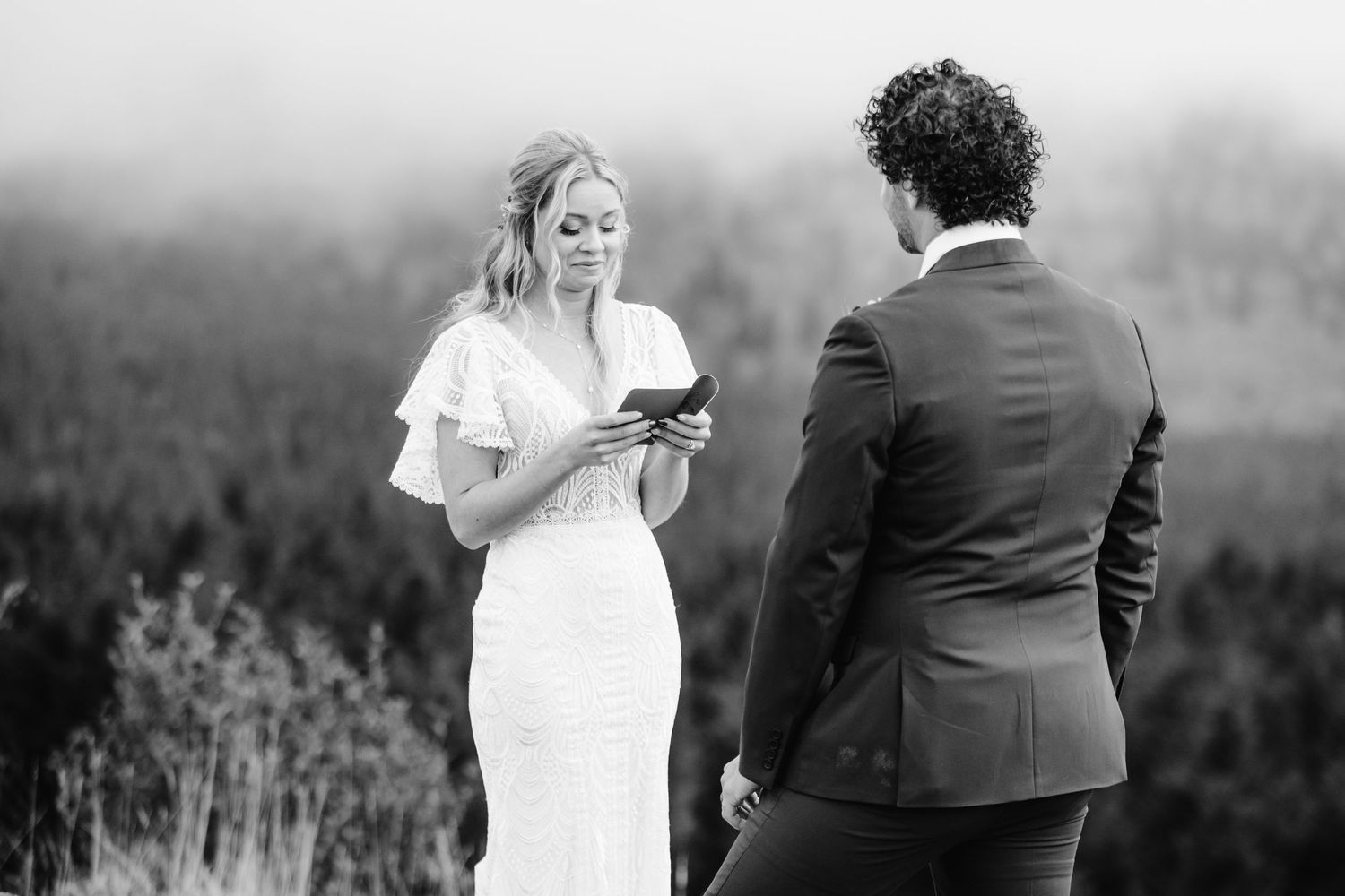 A couple reads their vows during a misty mountaintop ceremony in black and white.