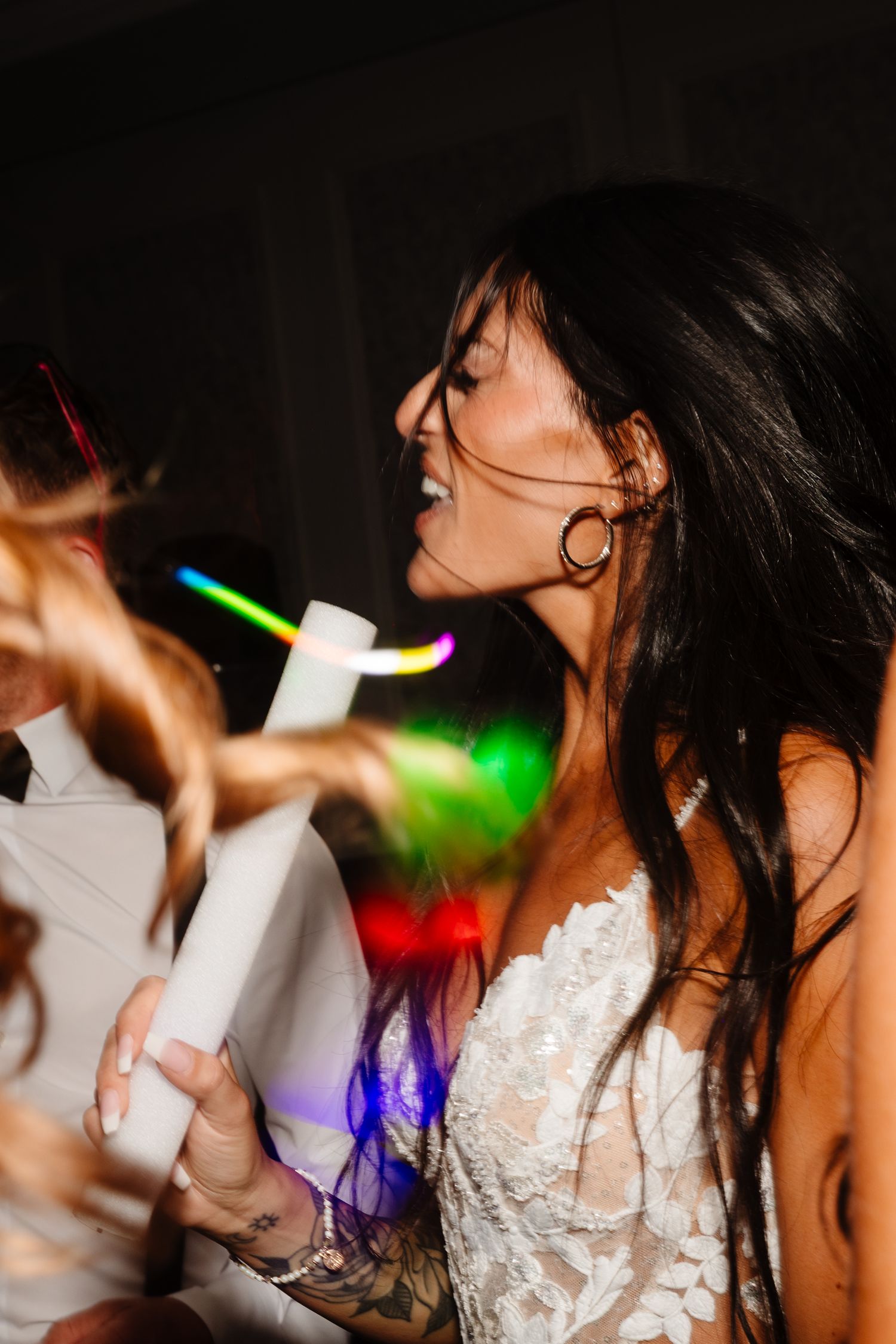 Bride dances with glowstick at nighttime wedding reception under colorful lights.