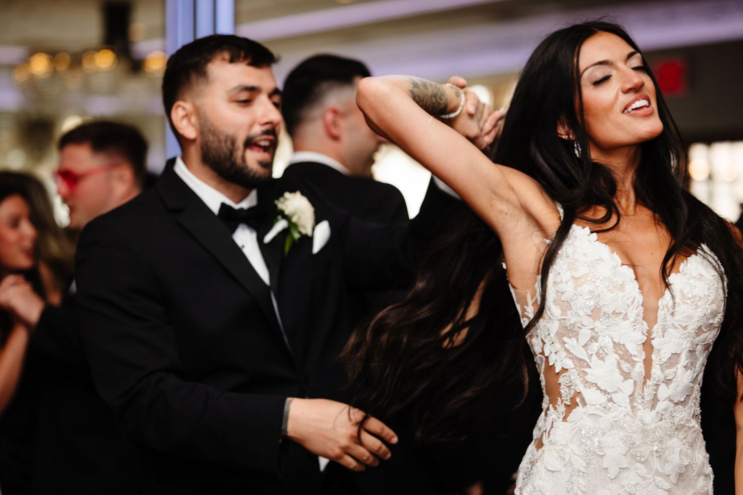 A bride in a lace wedding gown dances energetically with her groom at their reception.