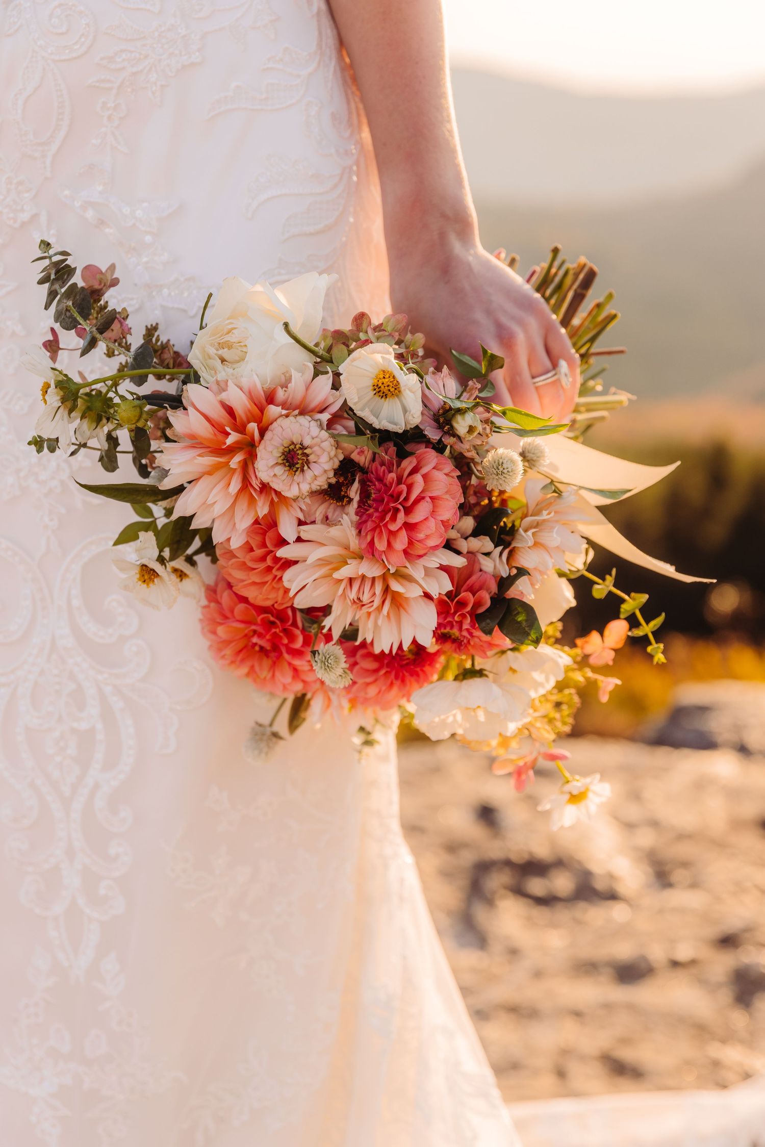 Stunning bridal bouquet with coral dahlias and white flowers against mountain backdrop at sunset.