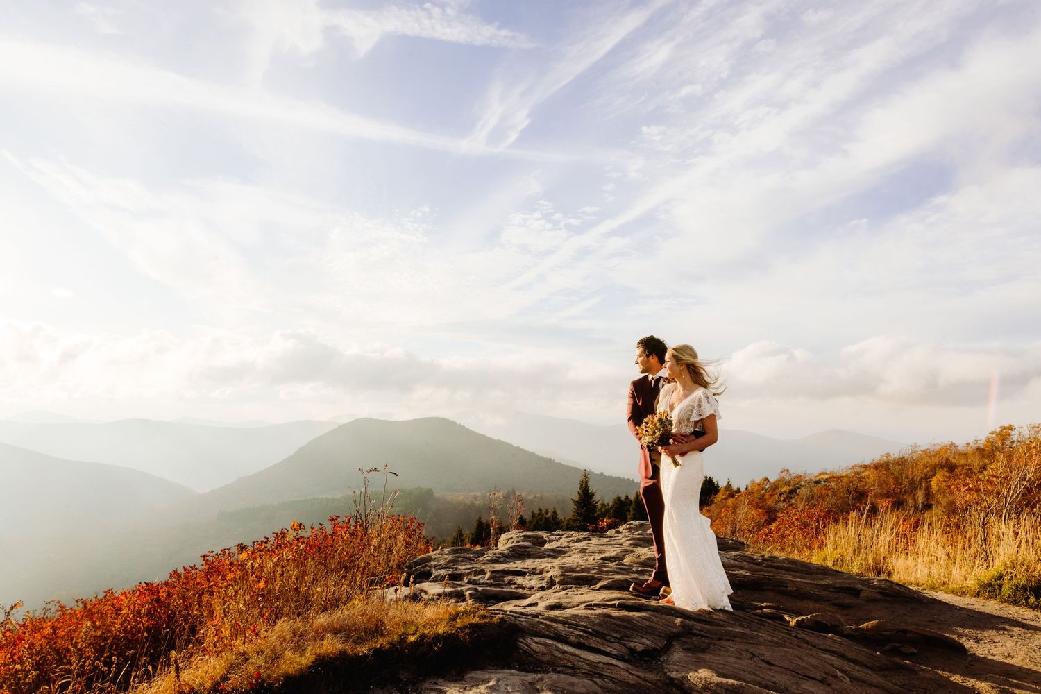 Wedding couple stands on a mountain peak surrounded by autumn colors and sweeping mountain vistas.