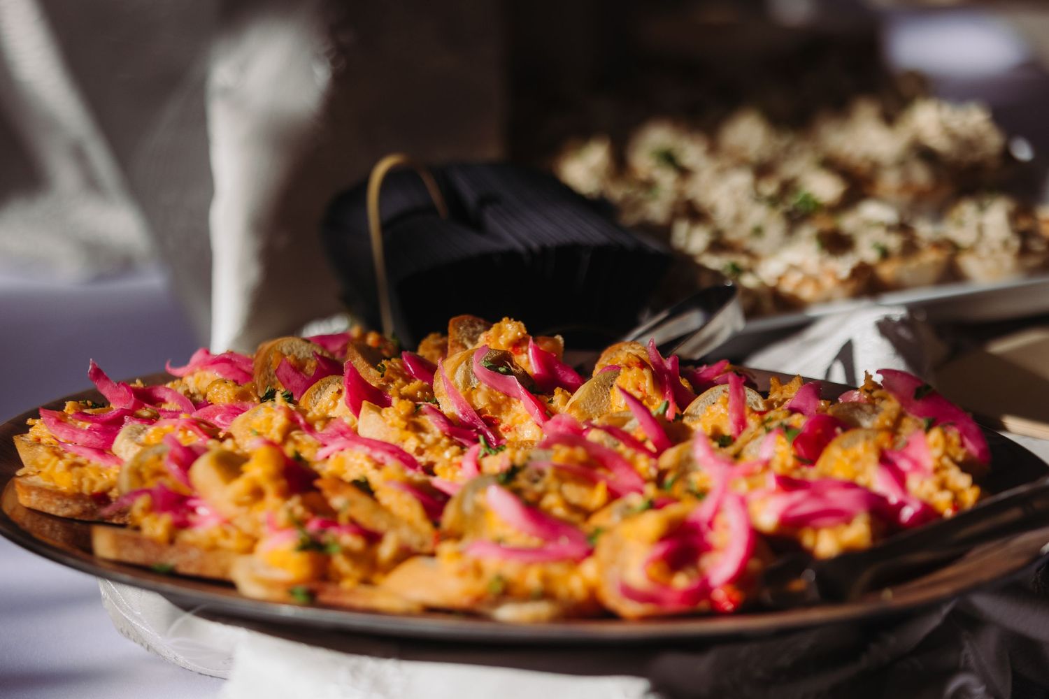 Colorful appetizers arranged in a row on dark plates with vibrant pink and orange garnishes.