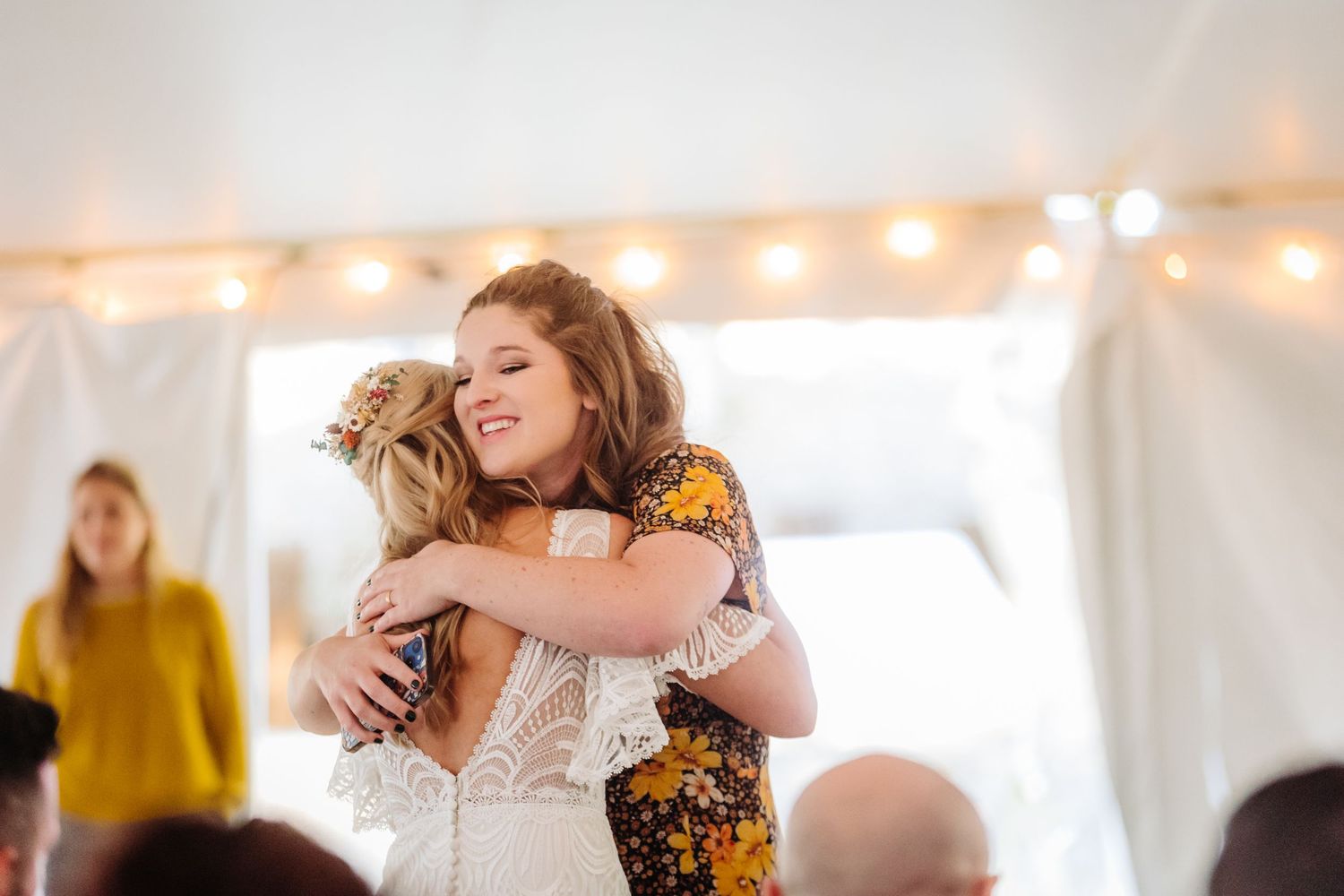 Two attendees share an emotional embrace during a wedding celebration under strings of lights.