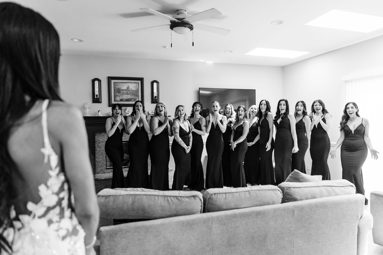 Wedding party members stand together against a white wall in formal attire.